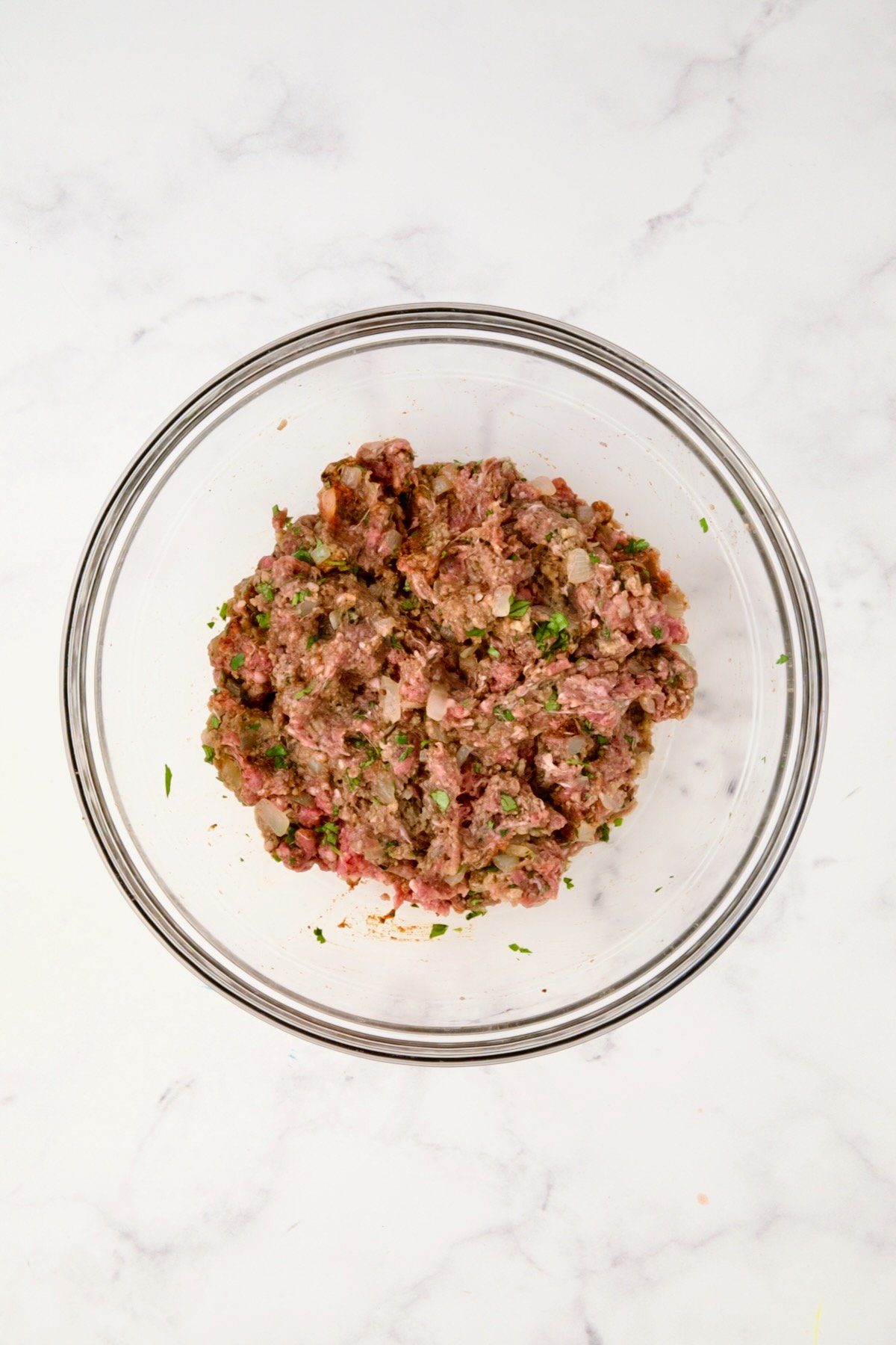 Ingredients for meatballs in glass bowl after being mixed together.