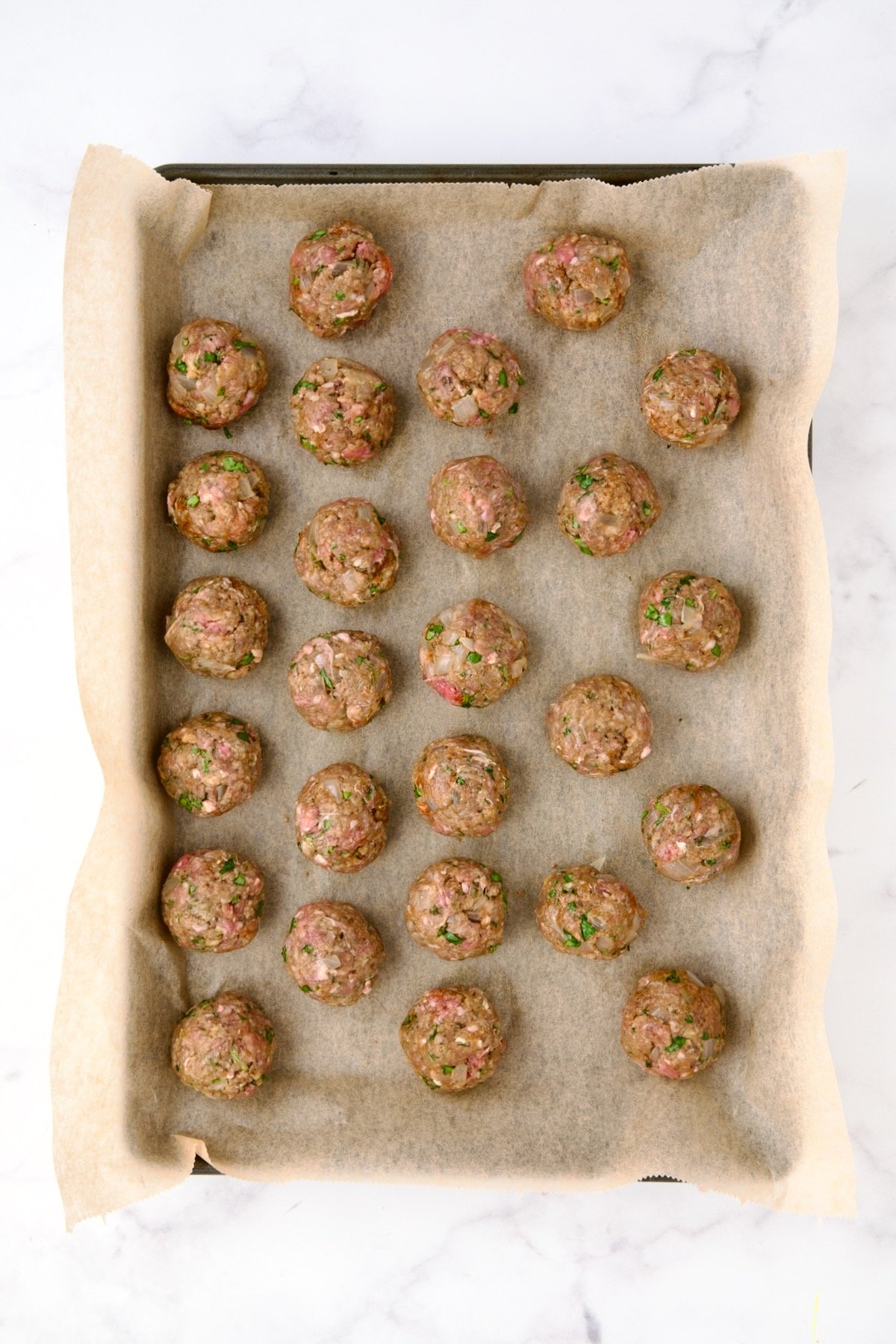 26 unbaked meatballs on parchment paper lined rimmed baking sheet.