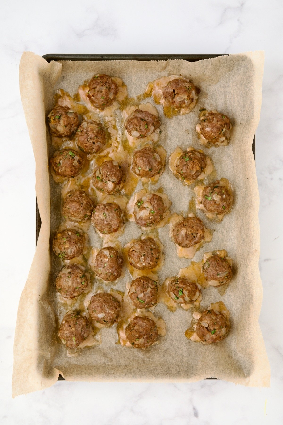 26 baked meatballs on parchment paper lined rimmed baking sheet.