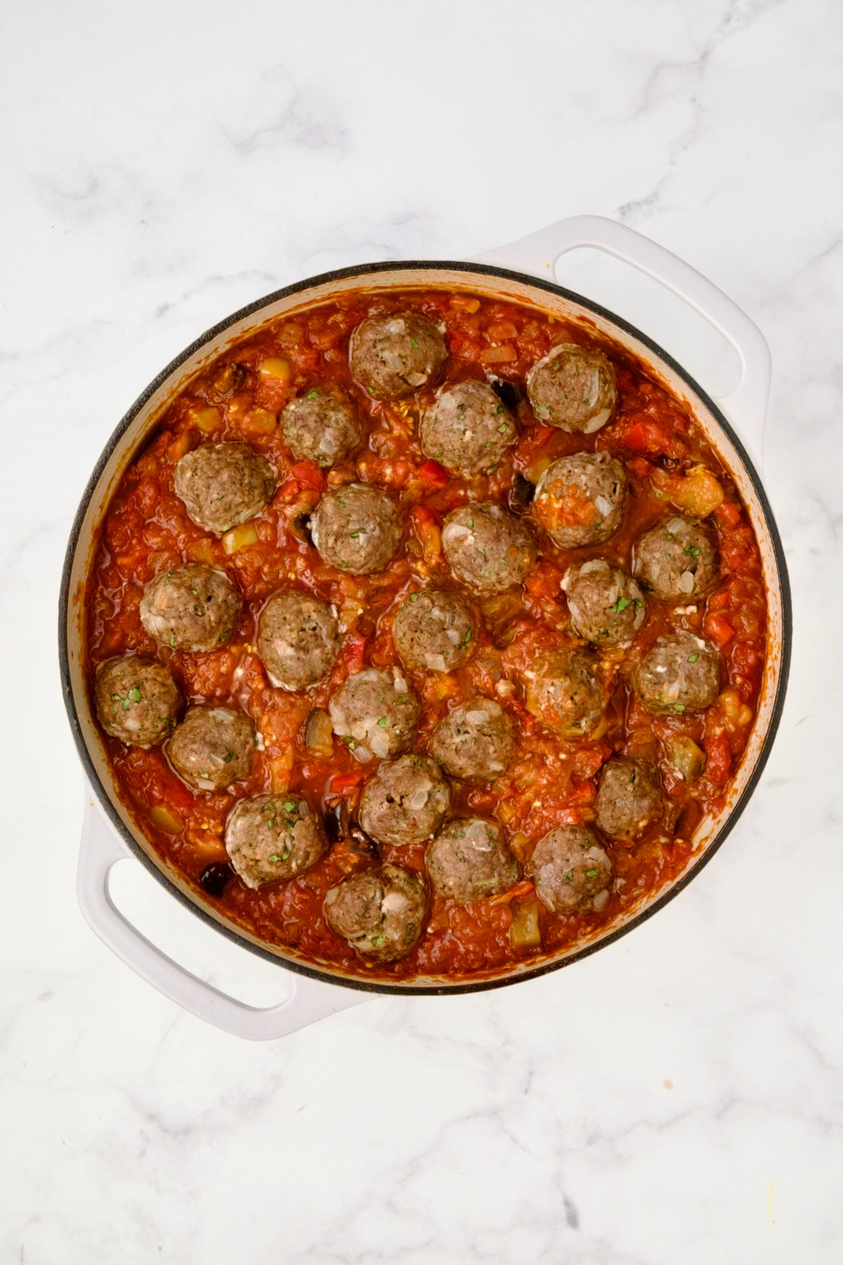 Meatballs added to finished sauce in white enamel cast iron skillet.