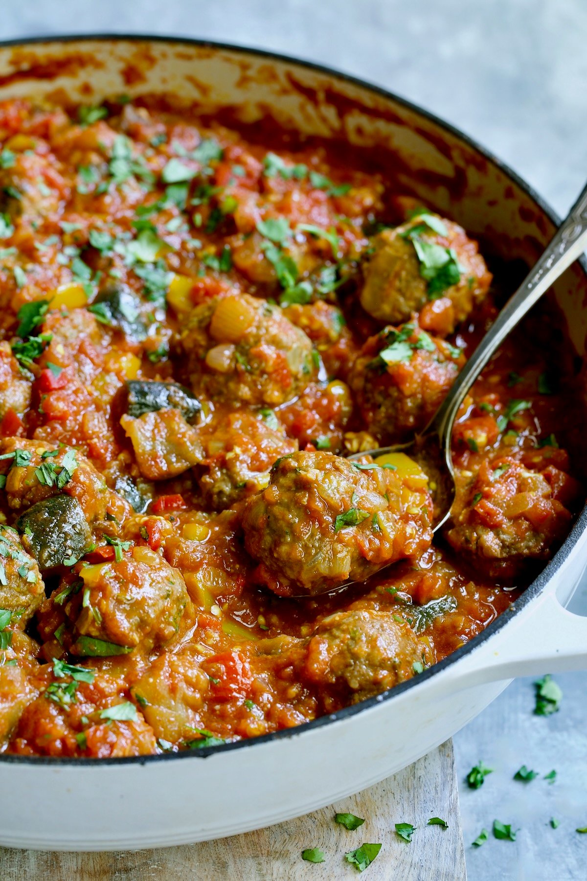 Moroccan Meatball Stew in white enamel cast iron skillet with serving spoon.