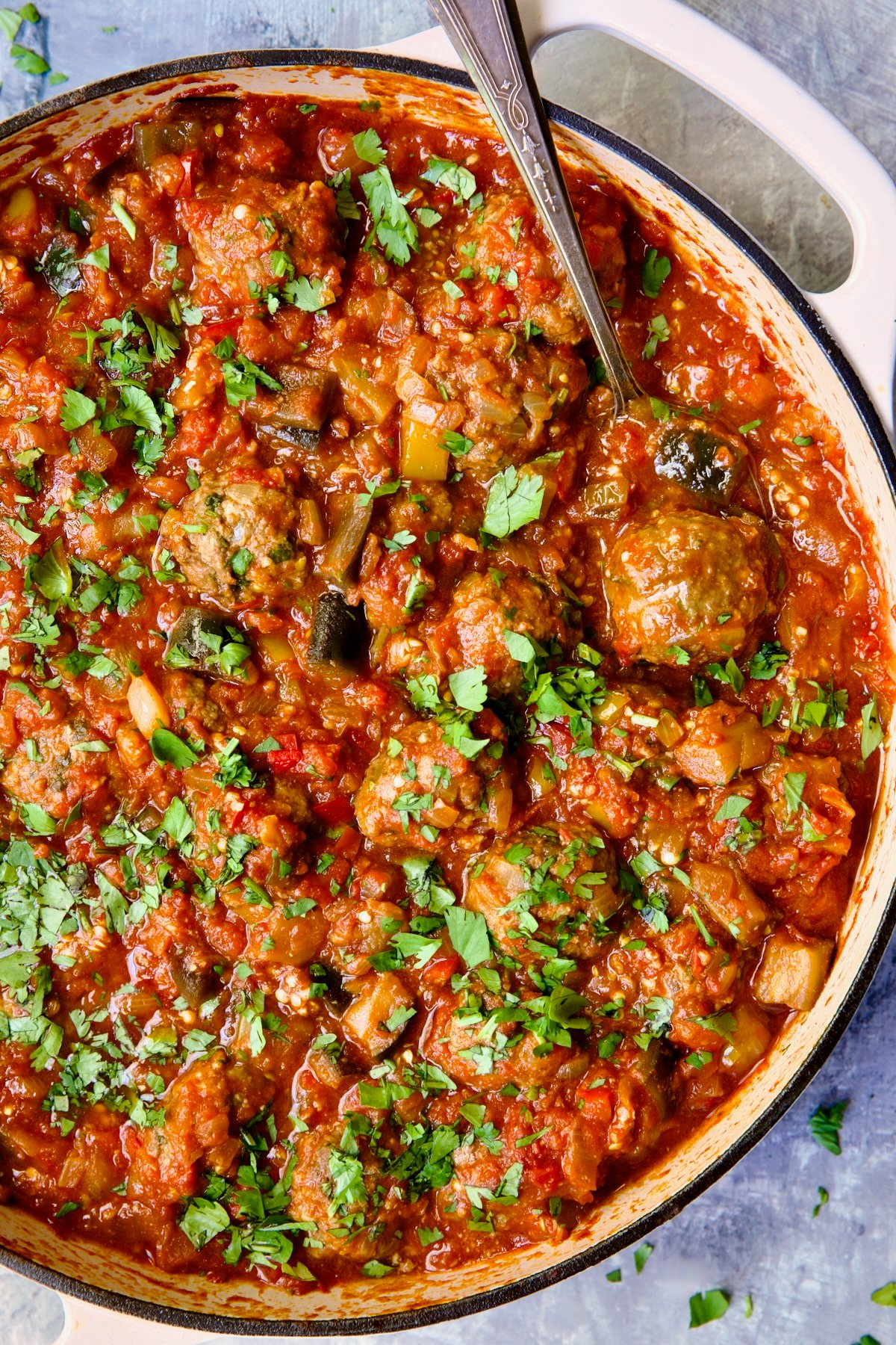 Moroccan Meatball Stew in white enamel cast iron skillet with serving spoon.