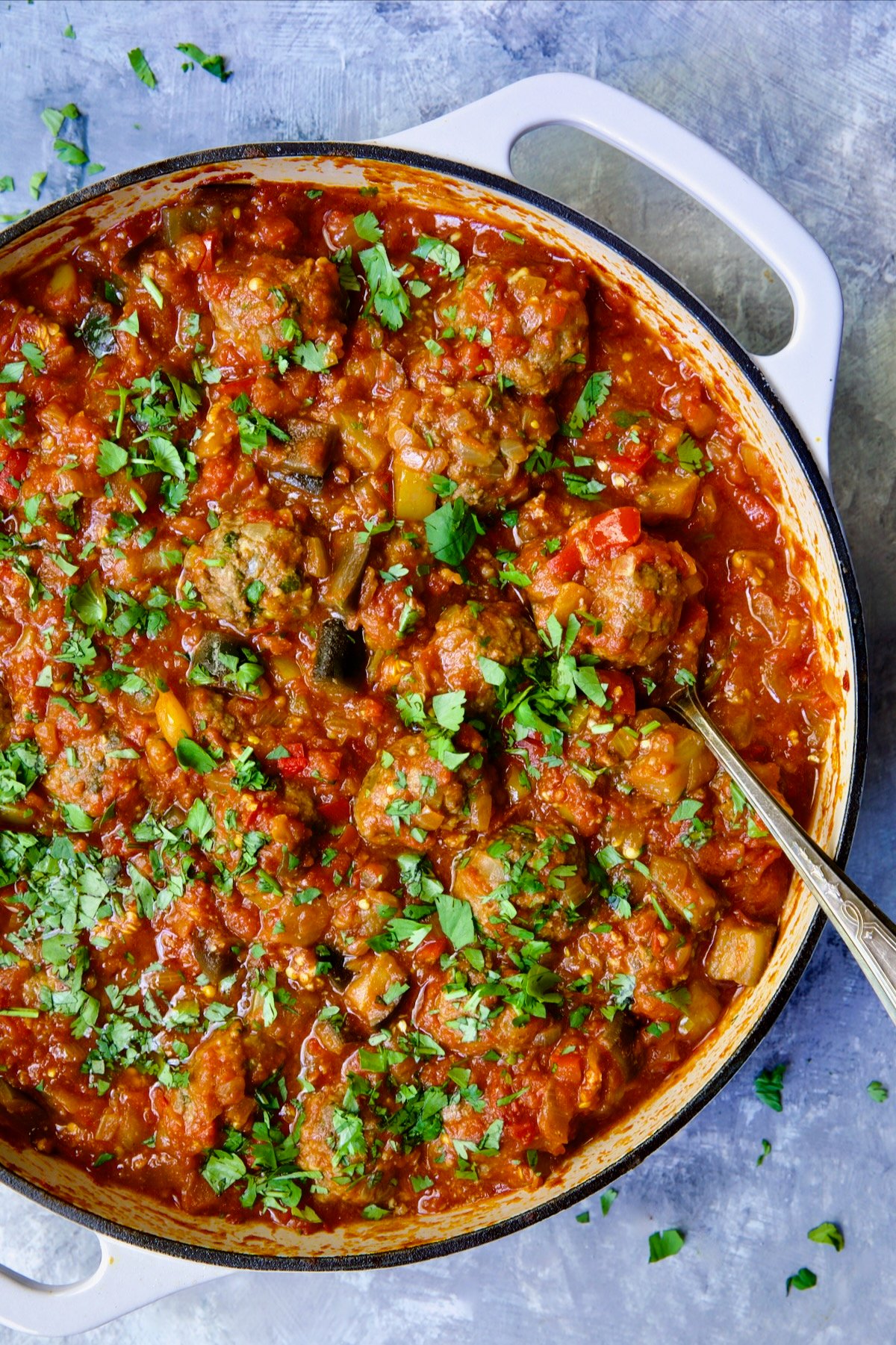 Moroccan Meatball Stew in white enamel cast iron skillet with serving spoon.