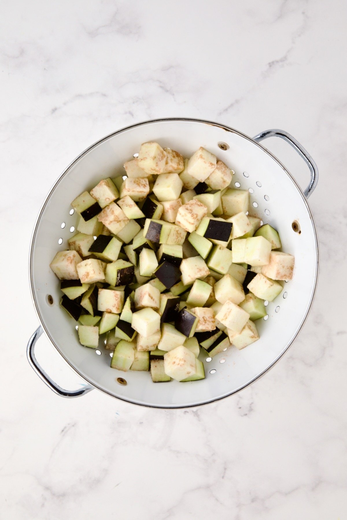 Cubed eggplant in white colander.