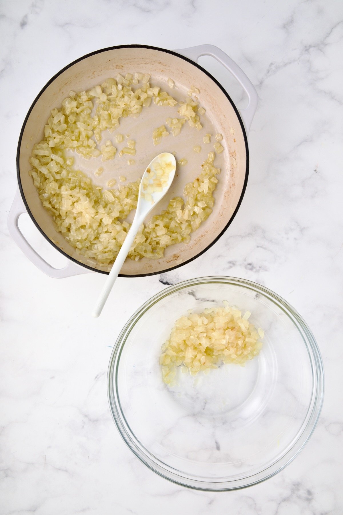 Cooked onions in white enamel cast iron with a third moved to a glass bowl.
