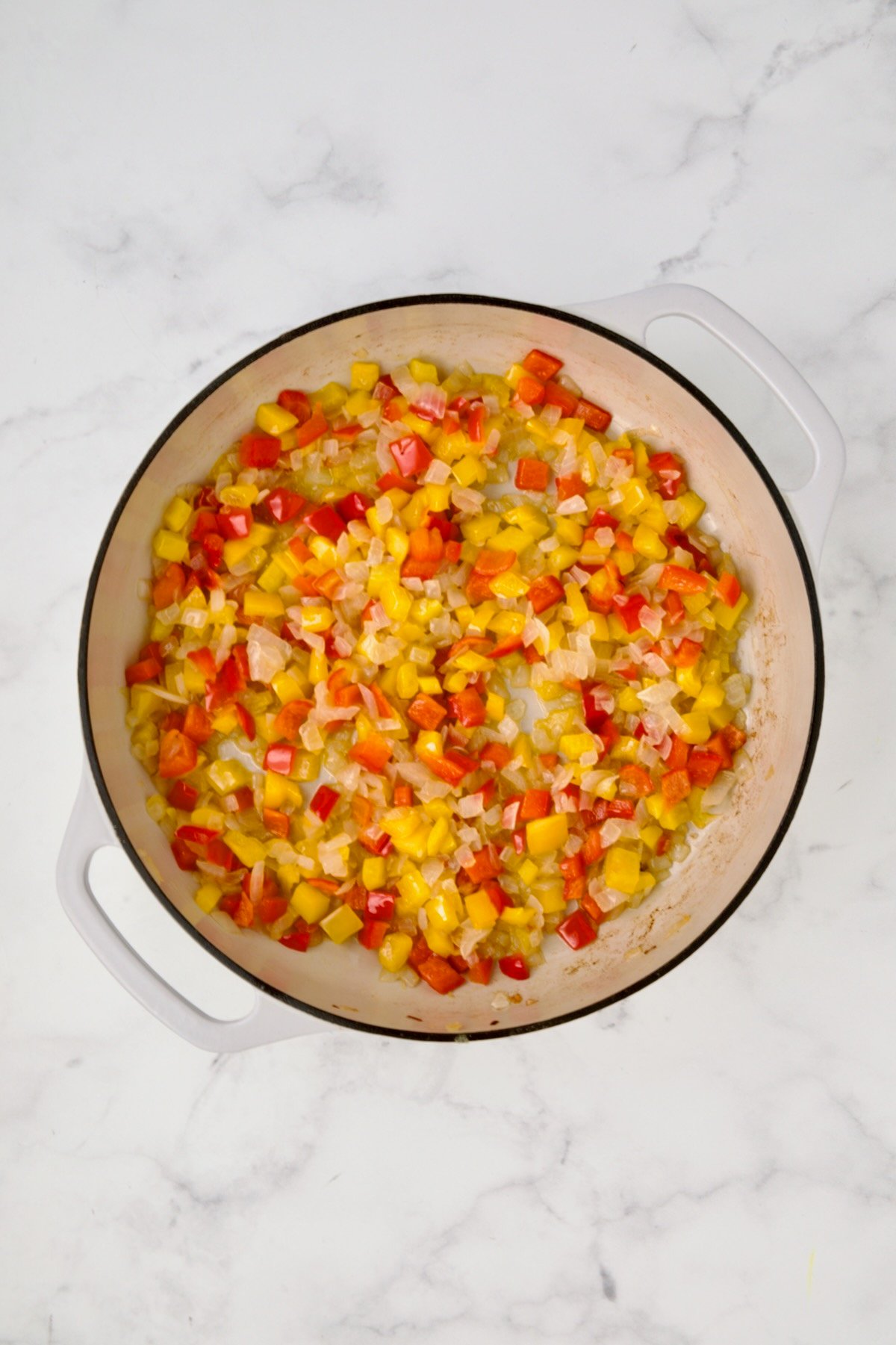 Cooked yellow bell peppers, red bell peppers and onions in white enamel cast iron skillet.
