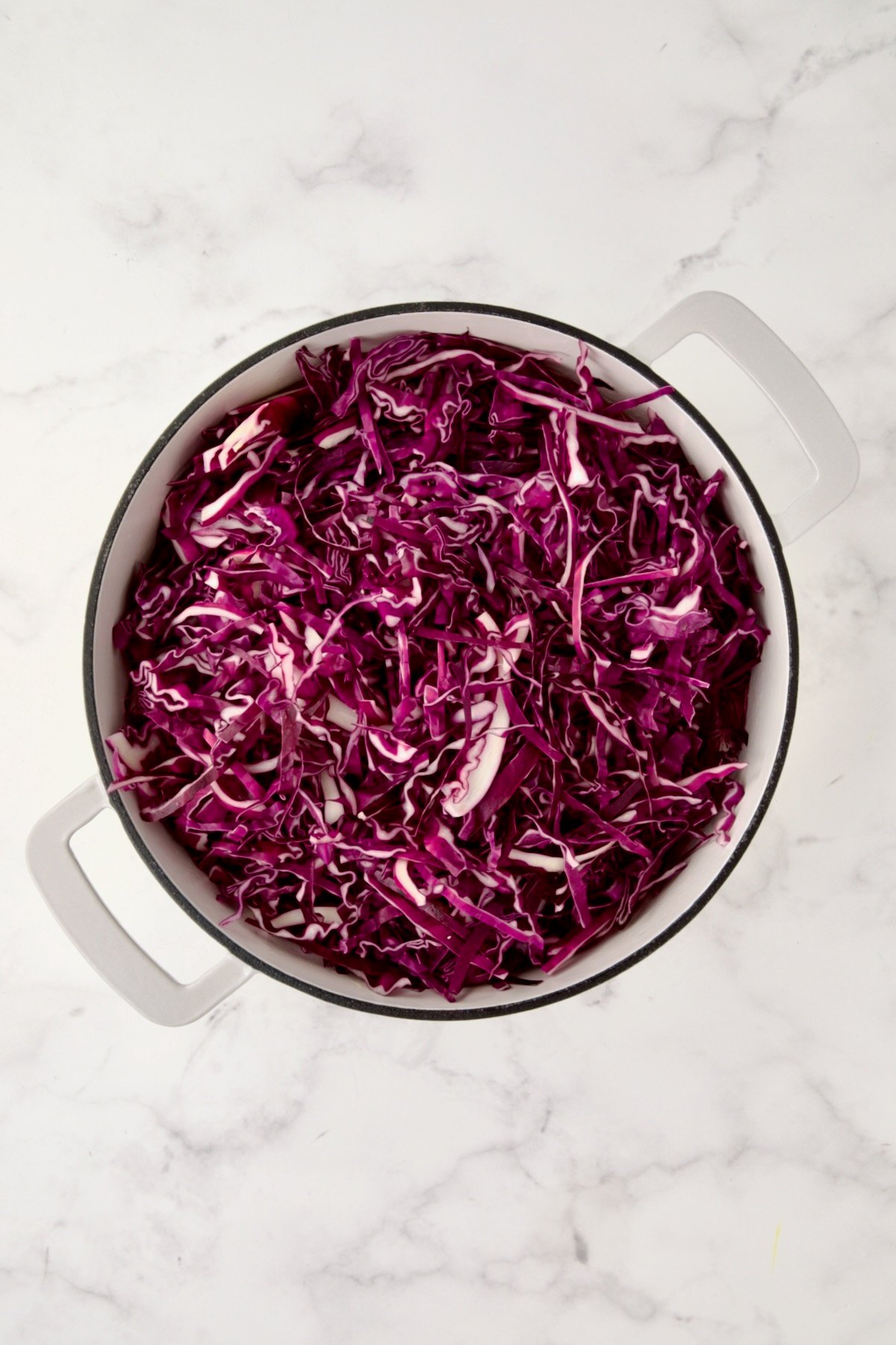 Uncooked cabbage added to white enamel cast iron skillet.