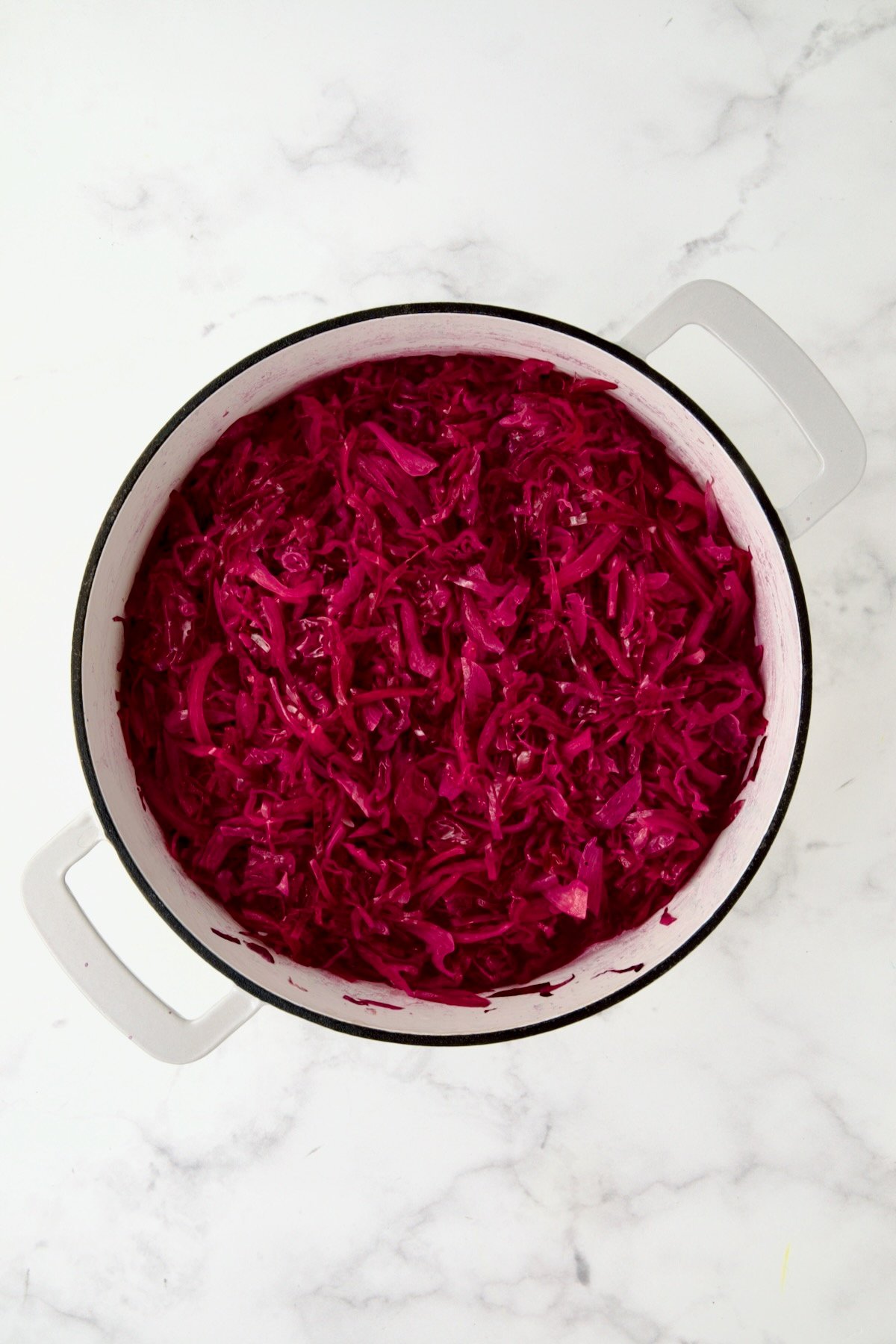 Partially cooked red cabbage in white enamel cast iron skillet.