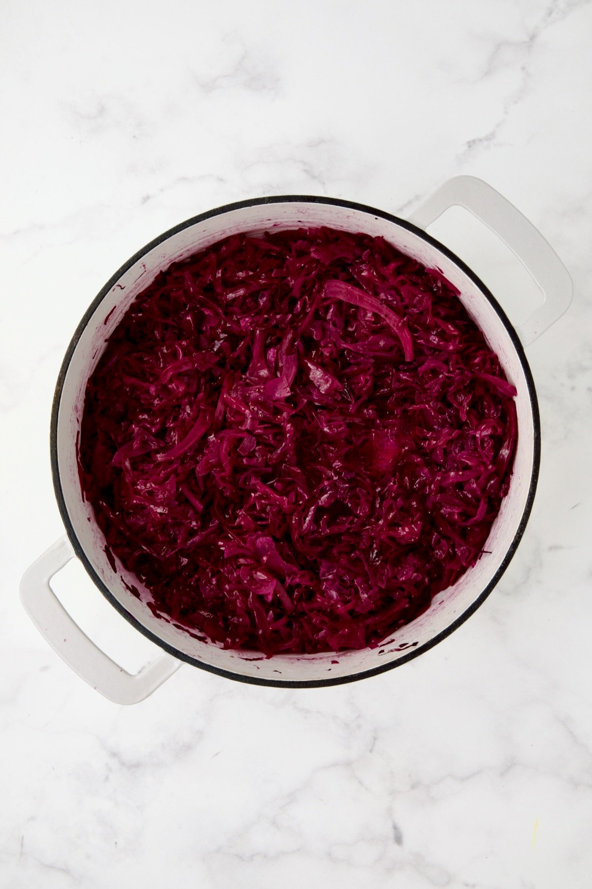 Fully cooked red cabbage in white enamel cast iron skillet.