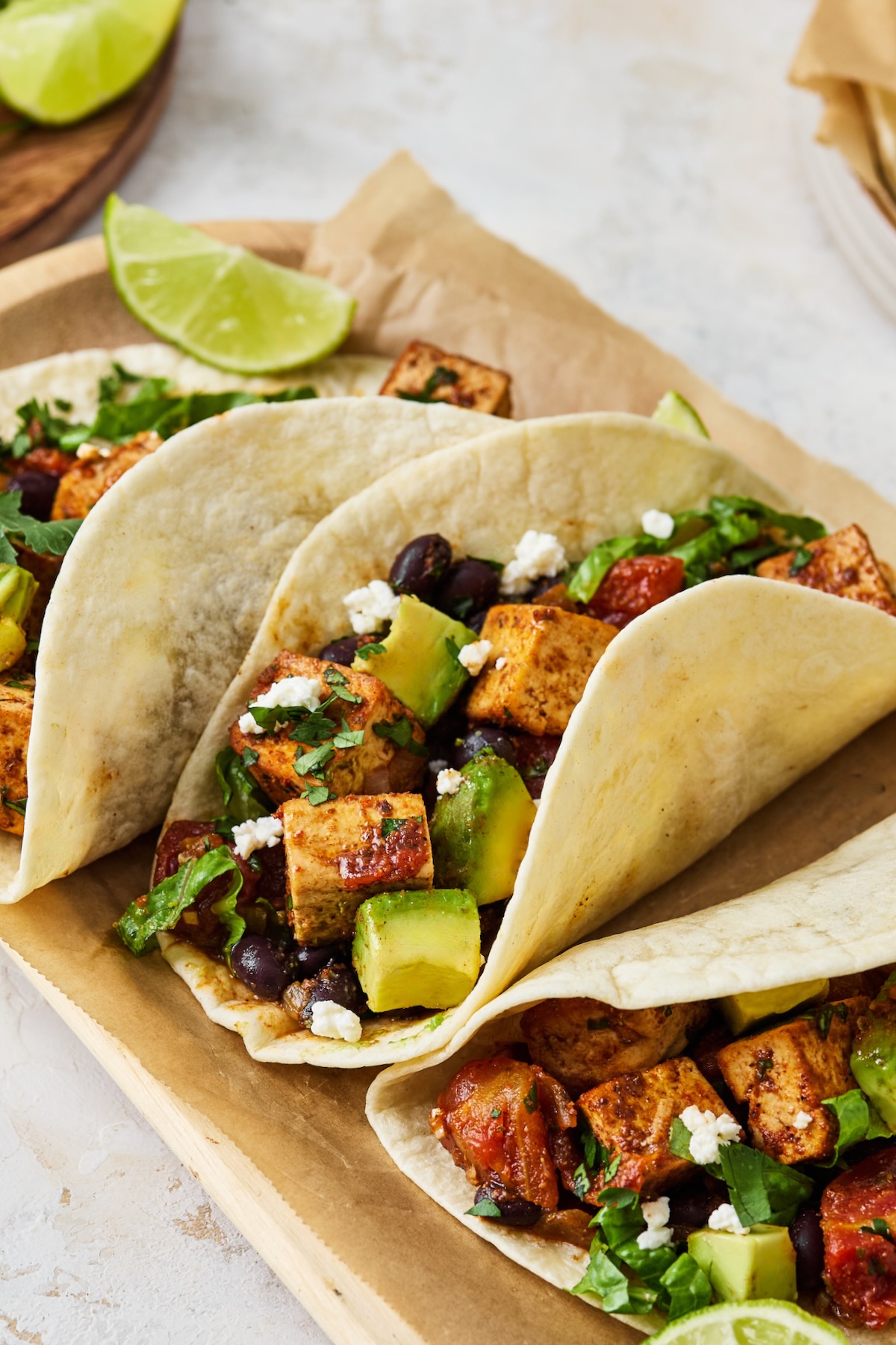 Three Tofu Black Bean Tacos on parchment paper lined wooden tray.