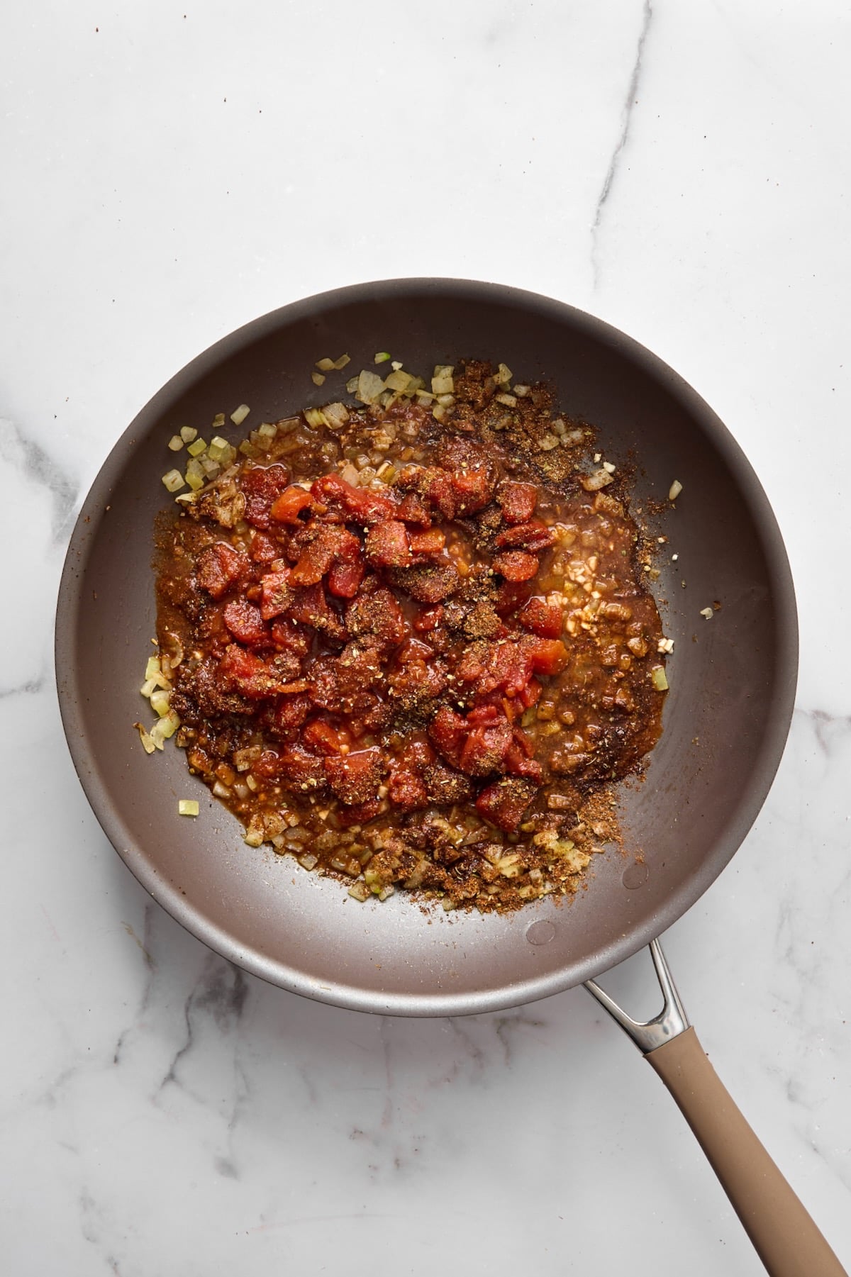 Diced tomatoes, garlic, and spices added to onions in nonstick skillet.