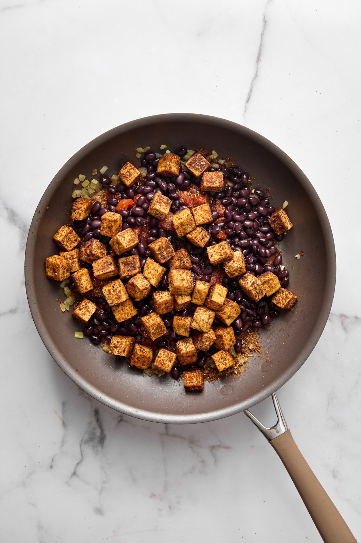Seared tofu cubes and black beans added to tomatoes and onions in nonstick skillet.