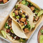 Three Tofu Black Bean Tacos on aluminum pan garnished with lime wedges.