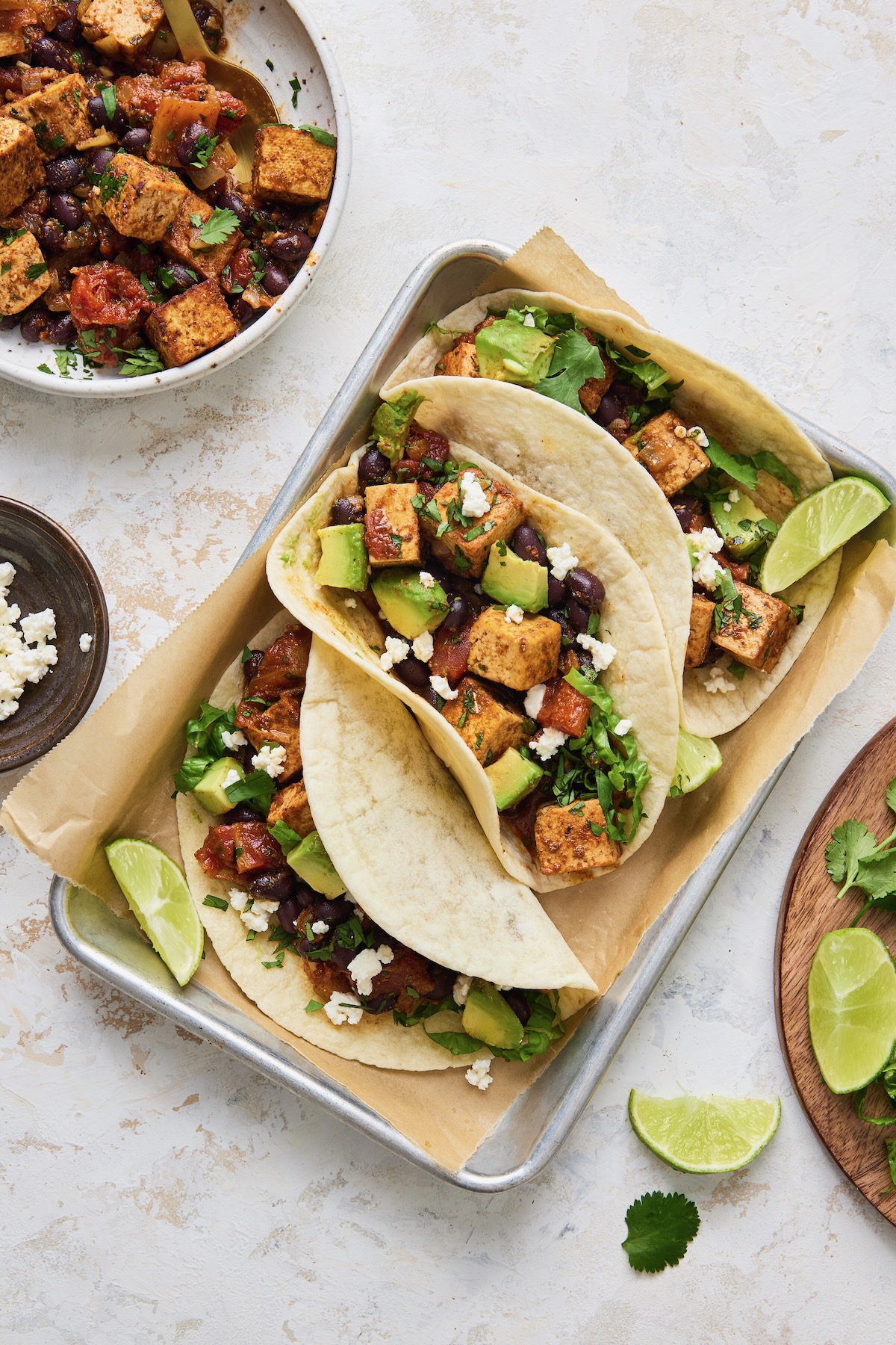 Three Tofu Black Bean Tacos on aluminum pan garnished with lime wedges.