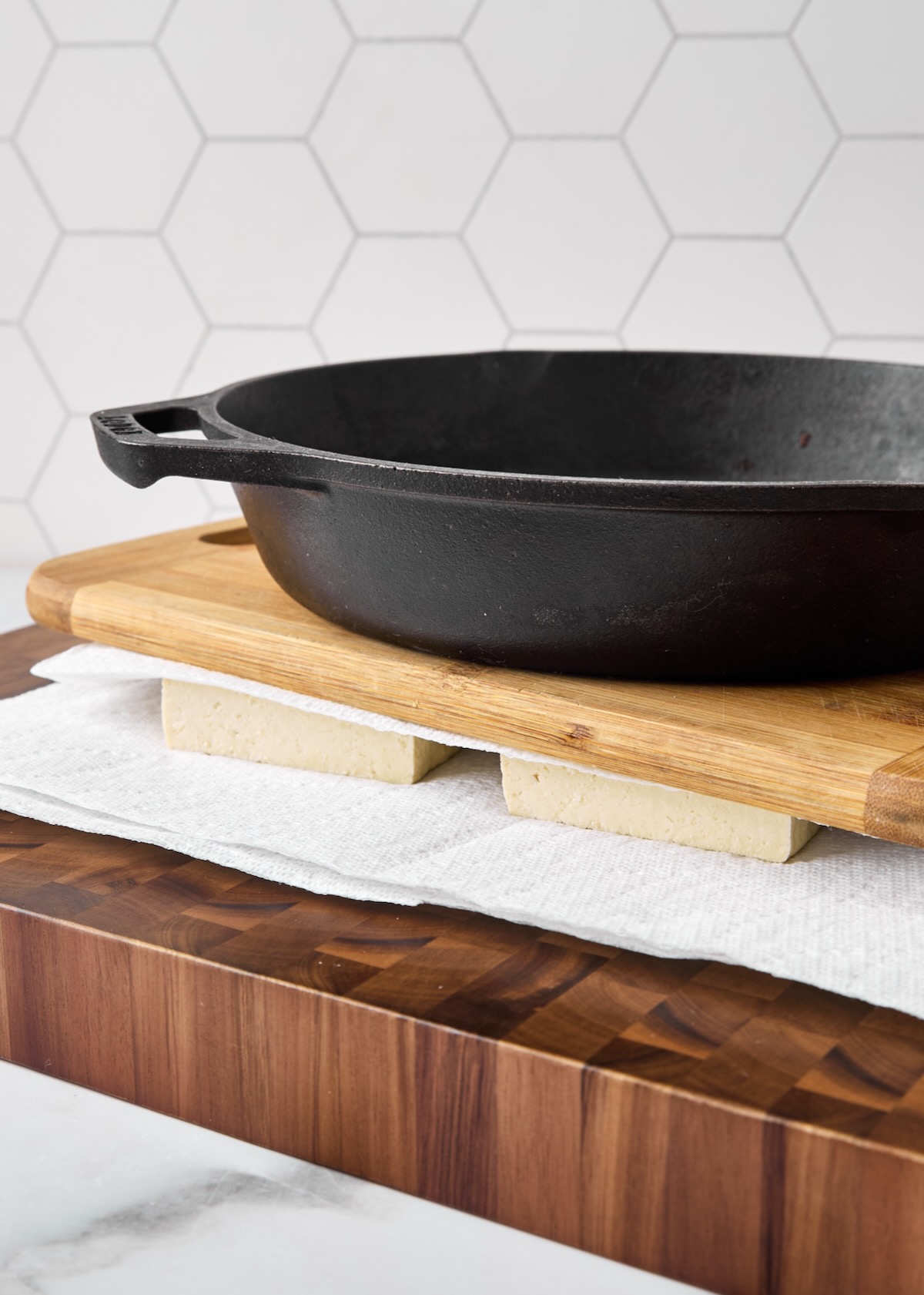 Cast-iron skillet set over tofu on wood cutting board.