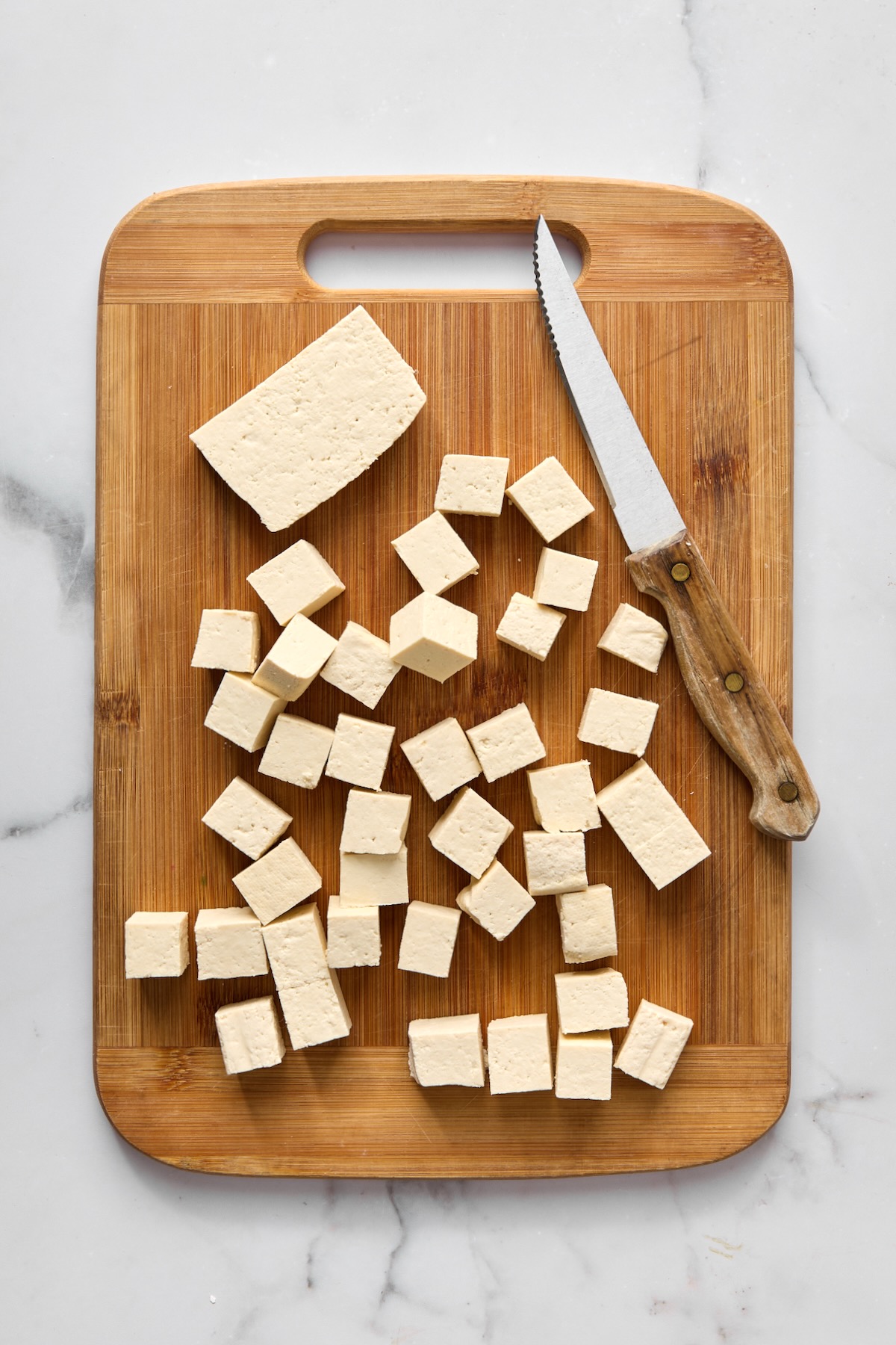 Cubed tofu and knife on bamboo cutting board.