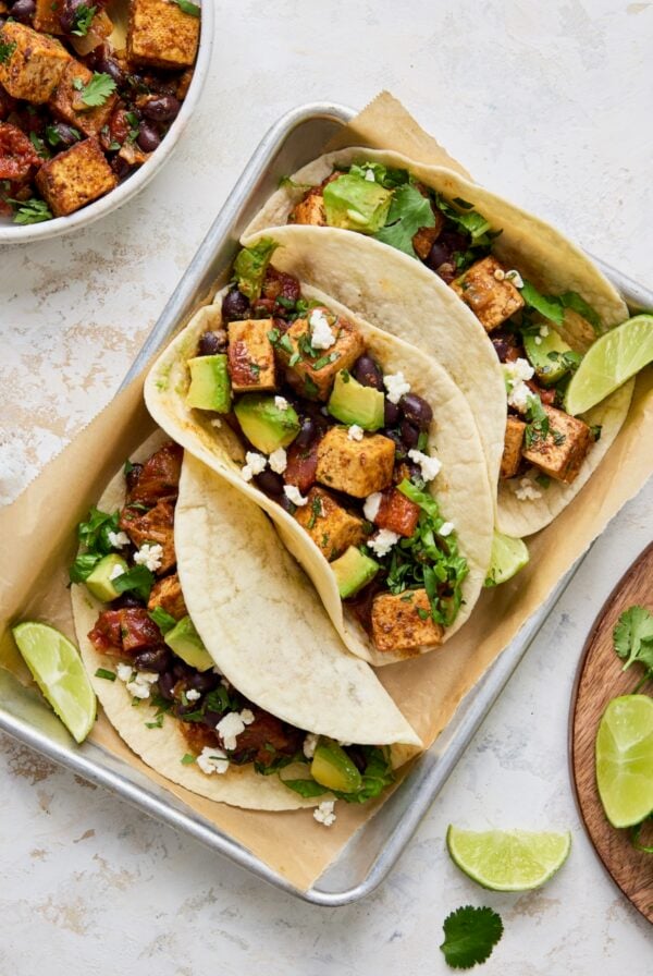 Three Tofu Black Bean Tacos on aluminum pan garnished with lime wedges.