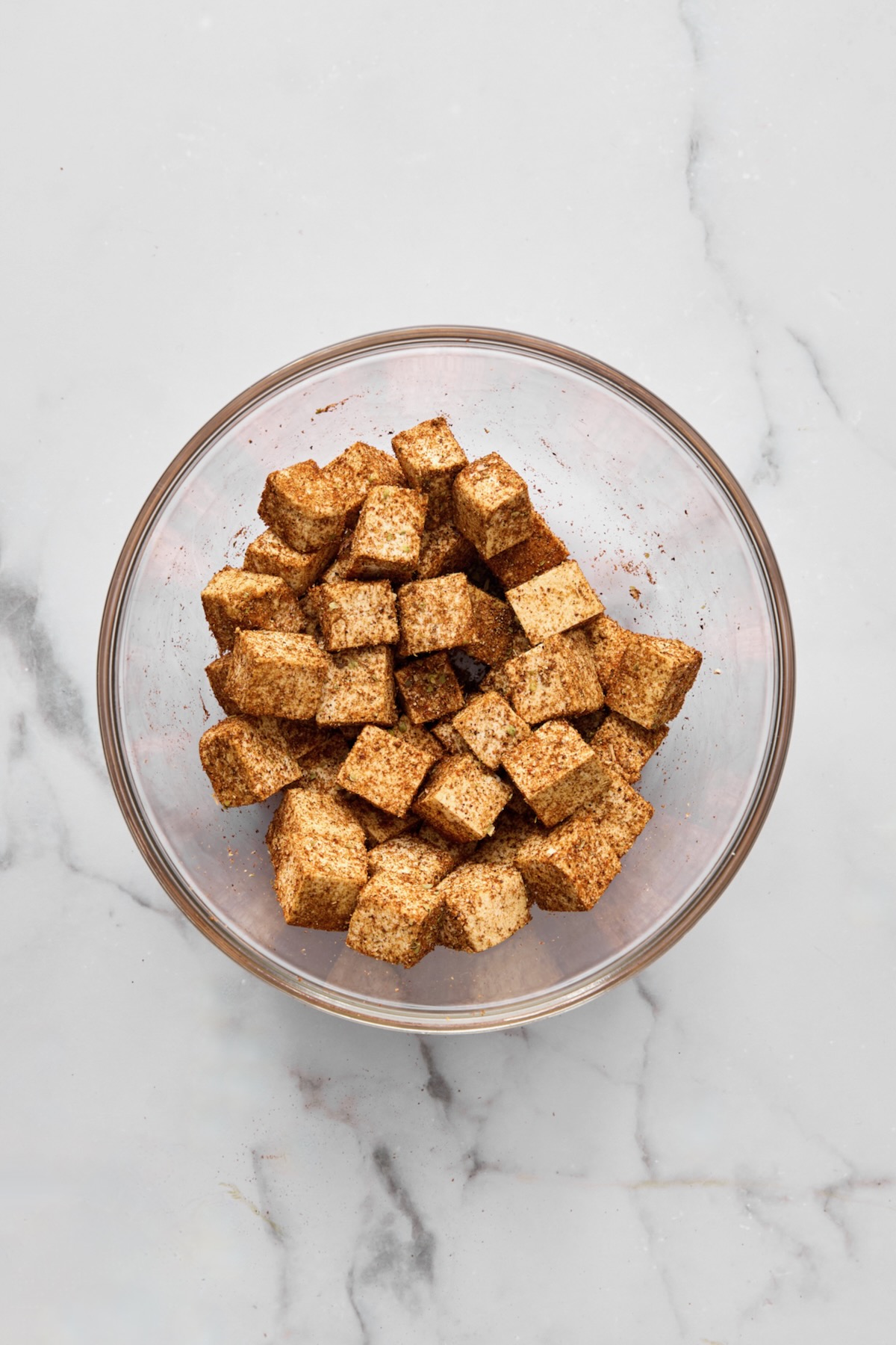 Cubes of tofu seasoned with spice blend in glass bowl.