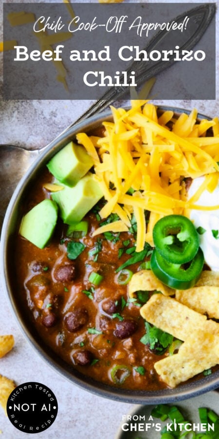 Pinterest graphic for Beef and Chorizo Chili showing one serving in a gray bowl garnished with avocado, cheddar, jalapeno, corn chips and sour cream.