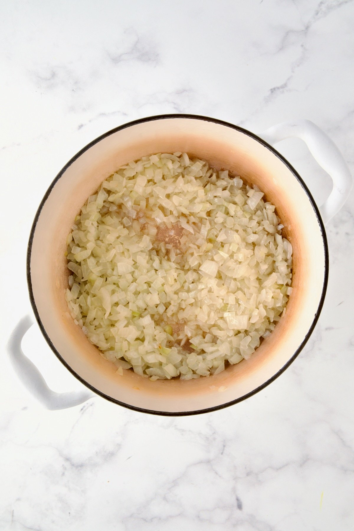 Cooked onions in white enamel Dutch oven.
