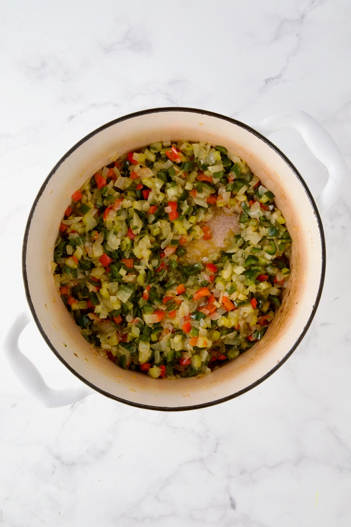 Cooked onions, celery and peppers in white enamel Dutch oven.
