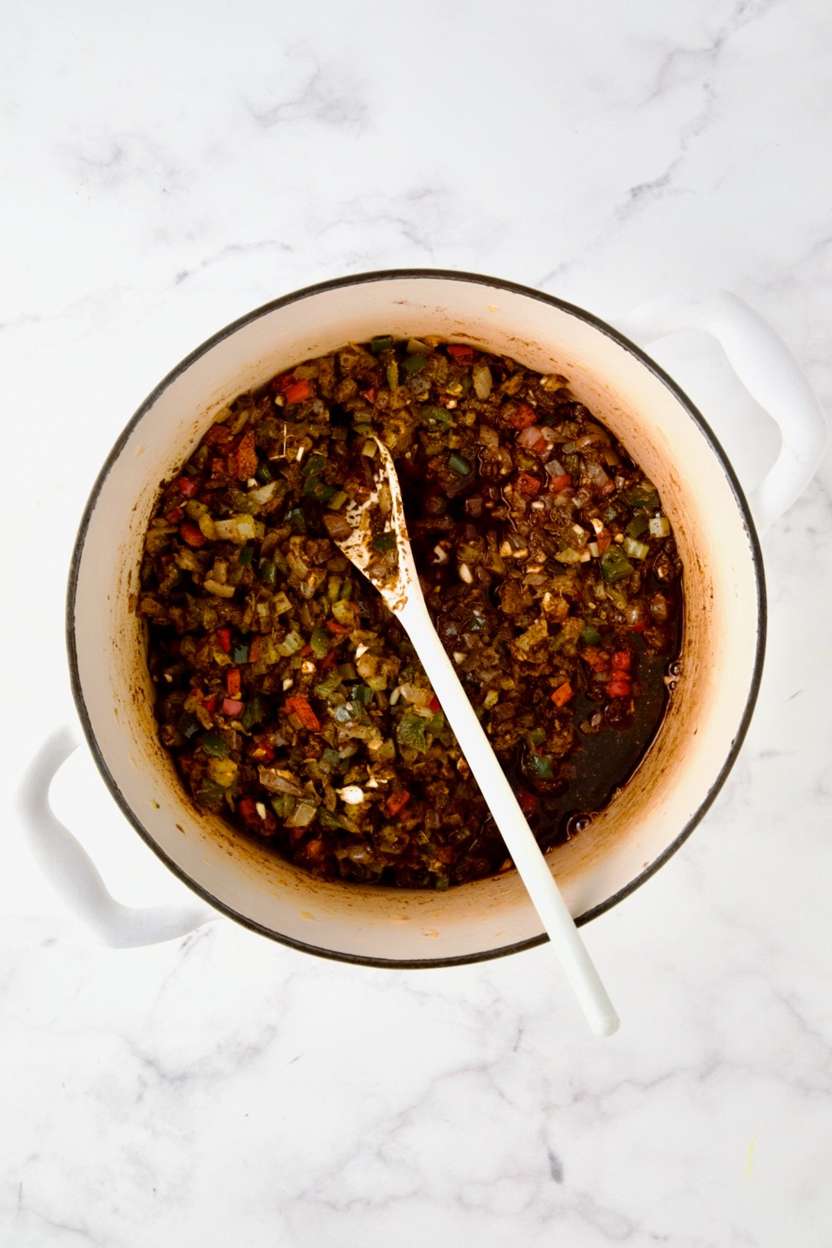 Wine added to spices and vegetables in white enamel Dutch oven.