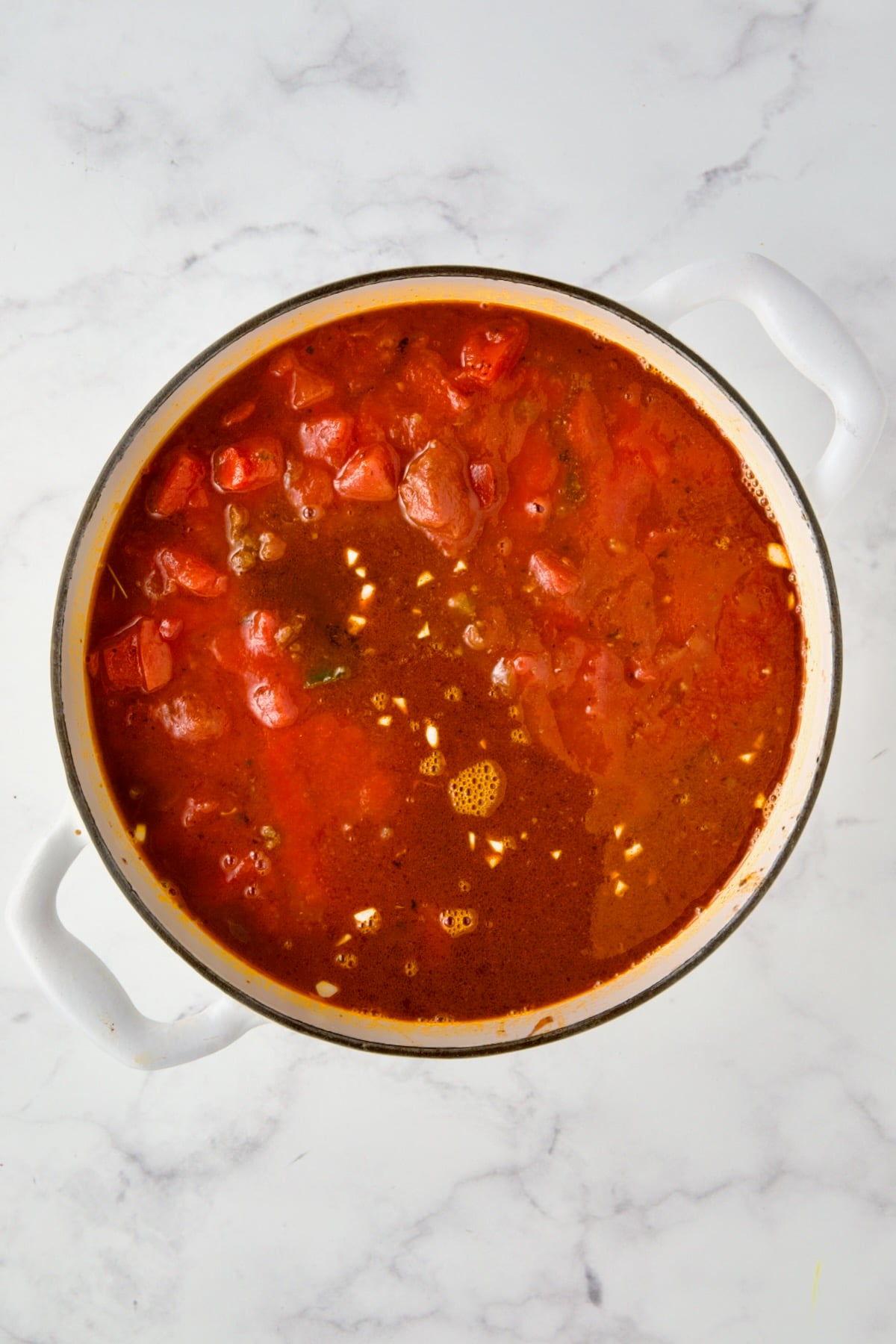 Tomatoes, tomato sauce and beef broth added to white enamel Dutch oven.