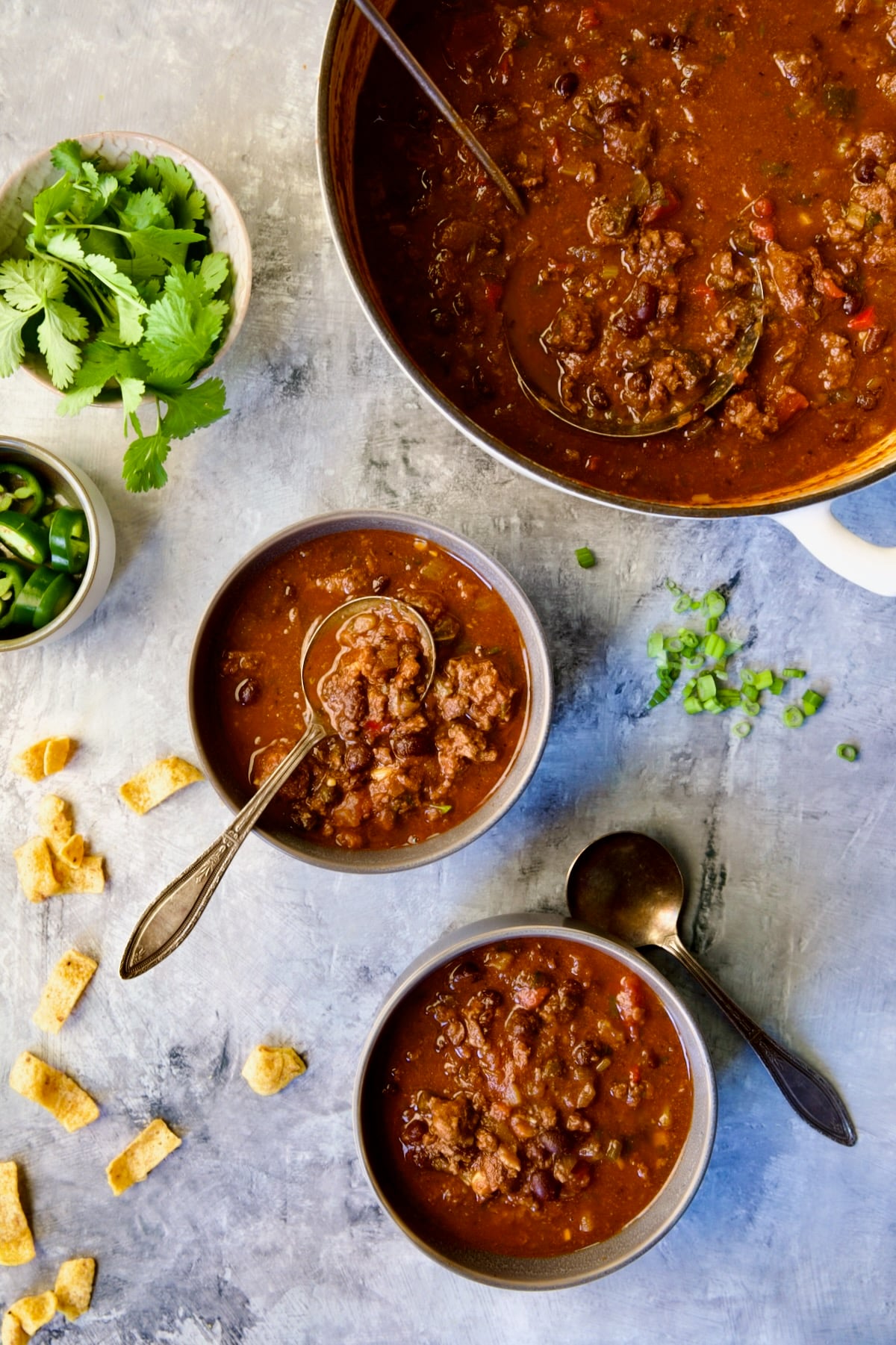 Beef and Chorizo Chili being dished up from white enamel Dutch oven into two gray bowls.