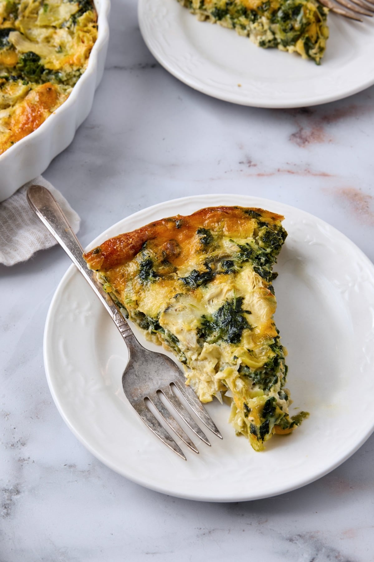 One piece of Crustless Spinach Artichoke Quiche on small white plate with fork.