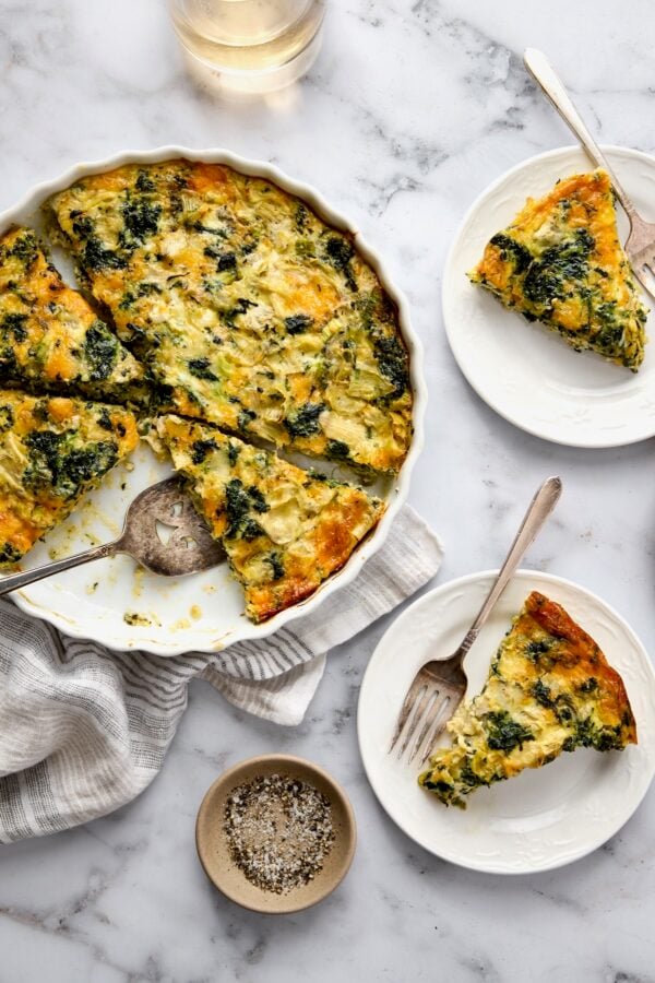 Crustless Spinach Artichoke Quiche with some in a white quiche pan and two pieces on small white plates.