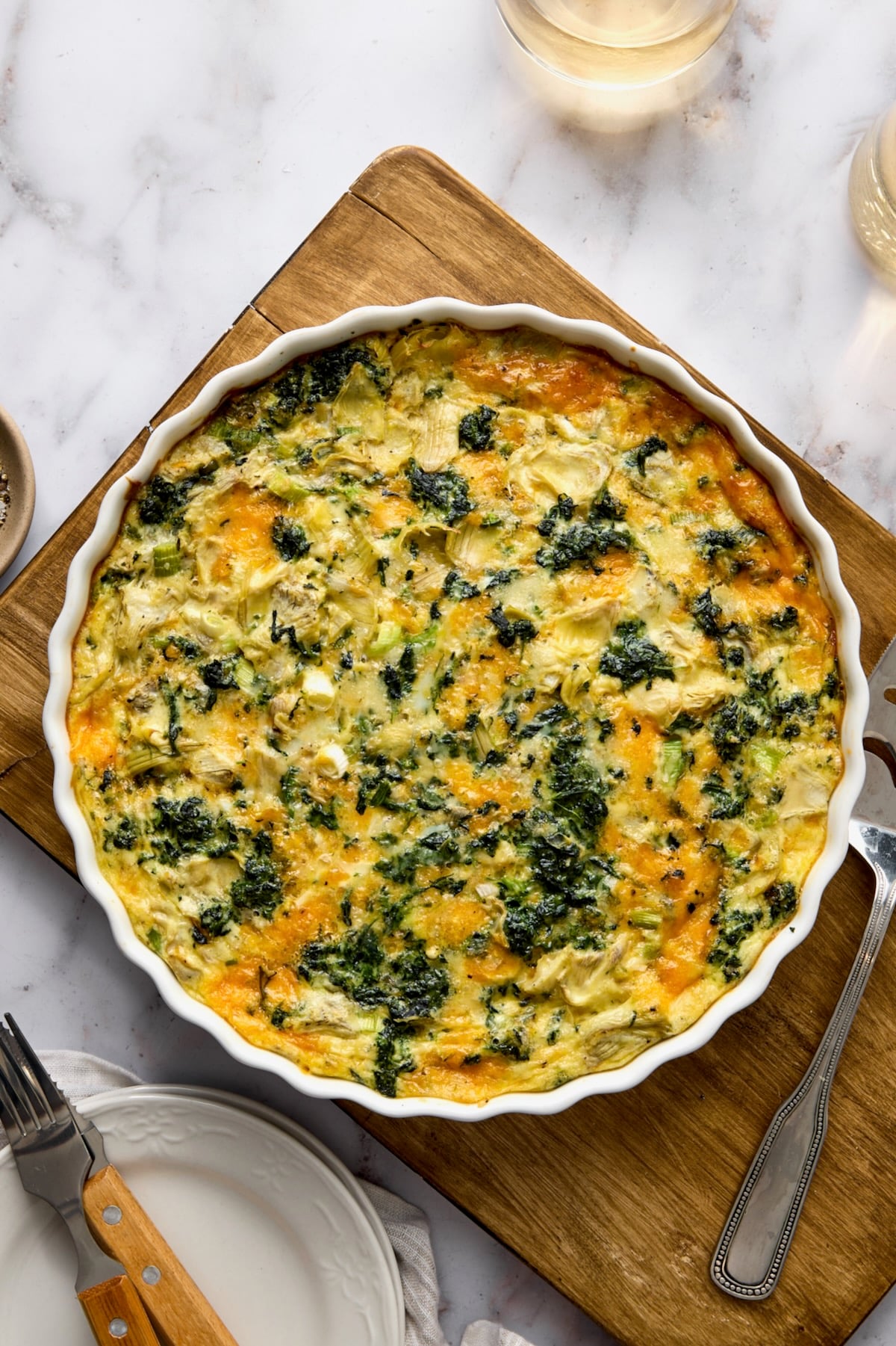 Crustless Spinach Artichoke Quiche on wood cutting board after being baked.