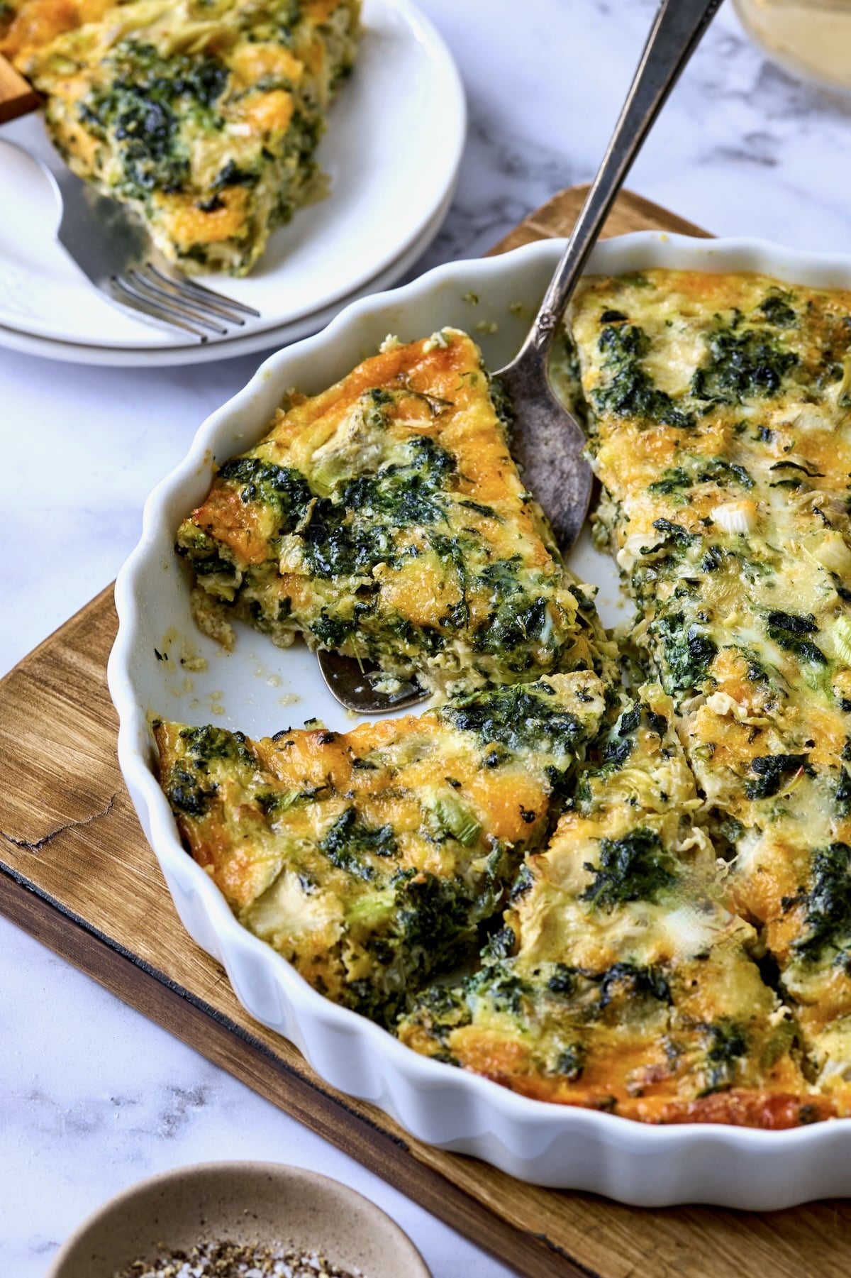 Crustless Spinach Artichoke Quiche with some in a white quiche pan and one piece on a small white plate.