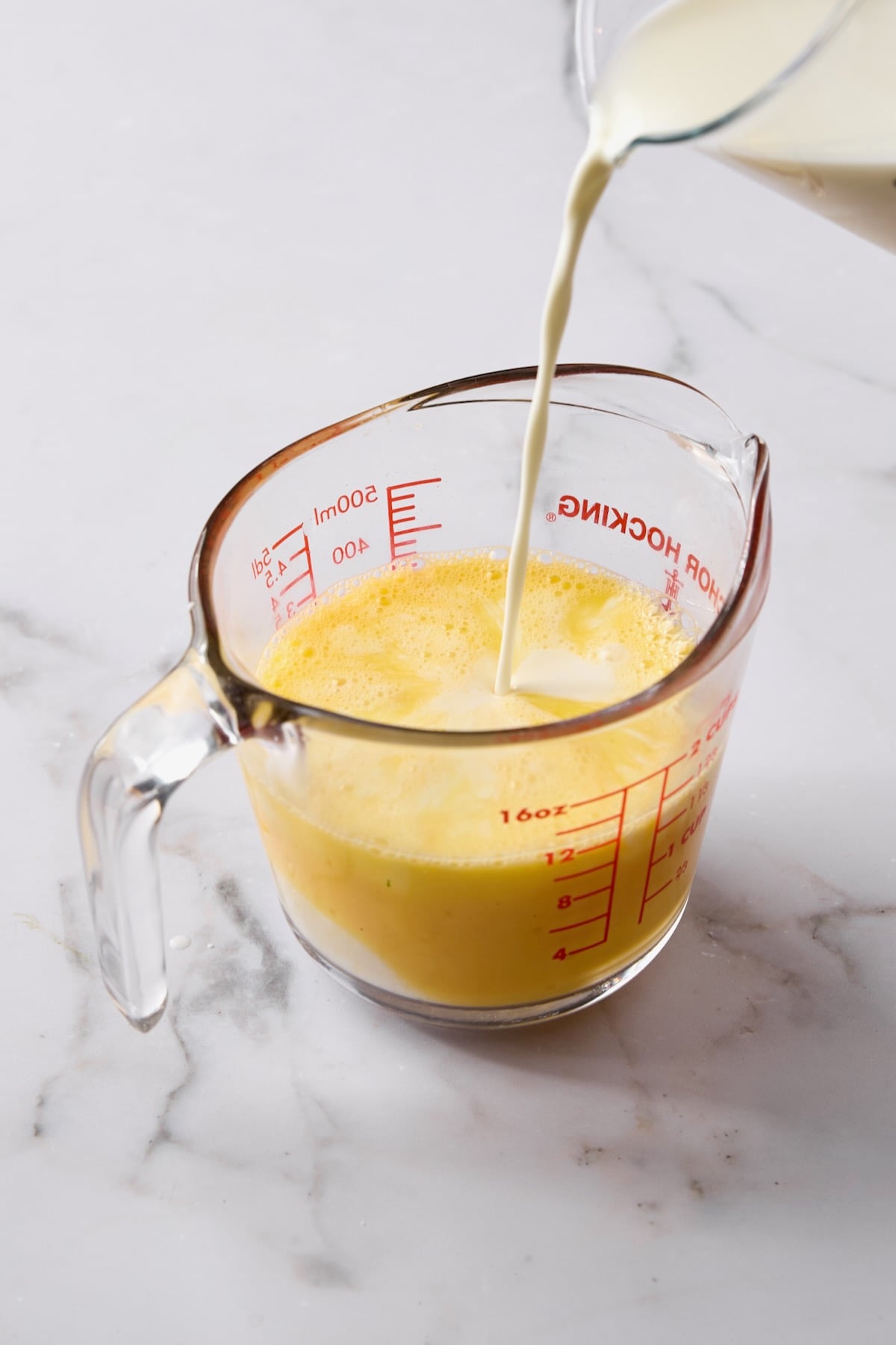 Custard being poured into eggs in glass measuring pitcher.