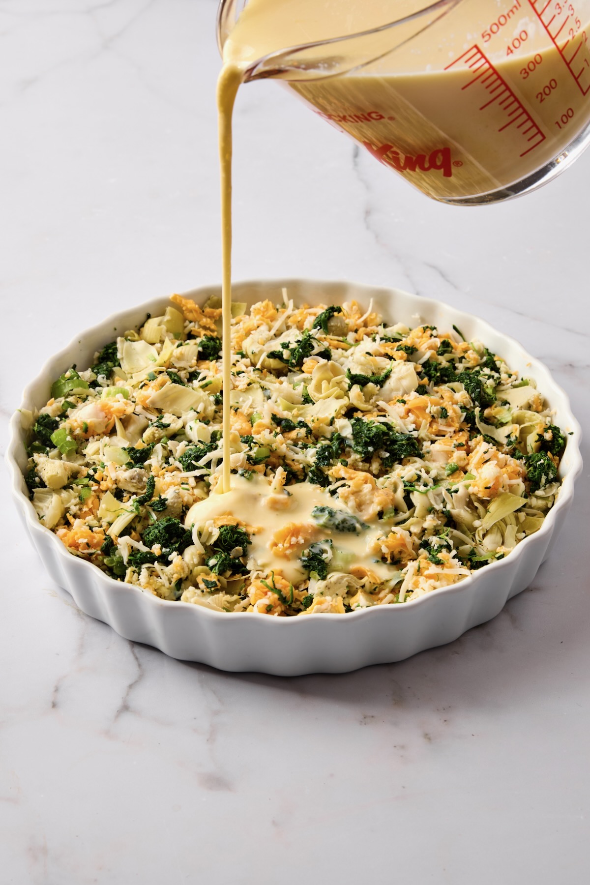 Glass measuring pitcher being poured into quiche.