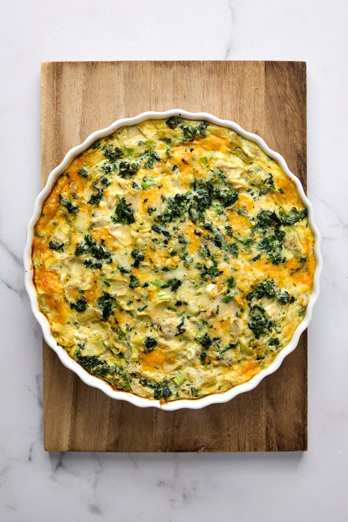 Crustless Spinach Artichoke Quiche on wood cutting board after being baked.