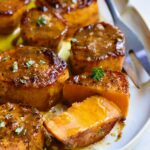Fondant Sweet Potatoes garnished with fresh thyme on white oval platter with one cut in half.
