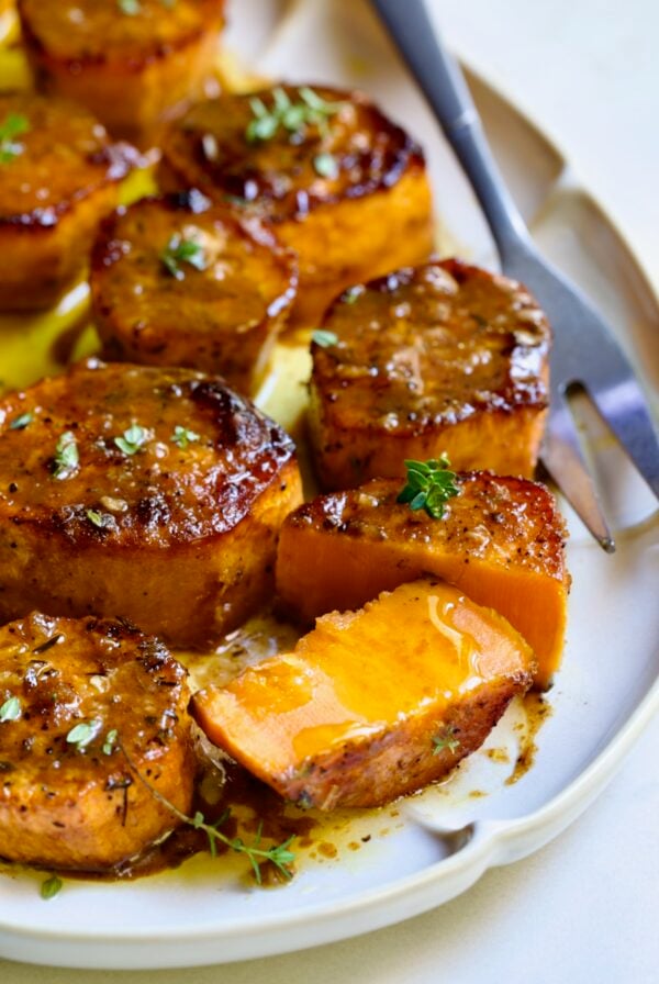 Fondant Sweet Potatoes garnished with fresh thyme on white oval platter with one cut in half.