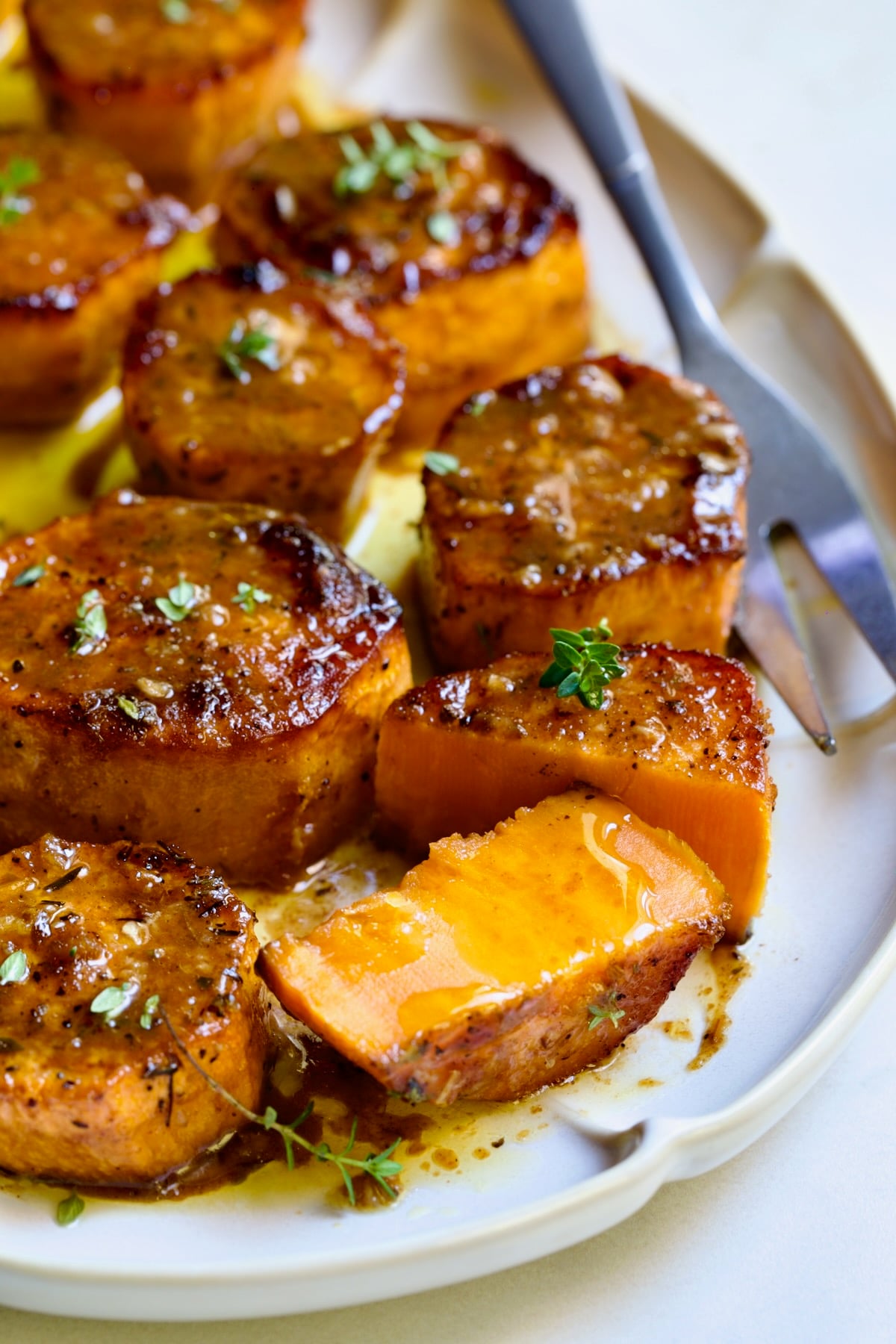 Fondant Sweet Potatoes garnished with fresh thyme on white oval platter with one cut in half.