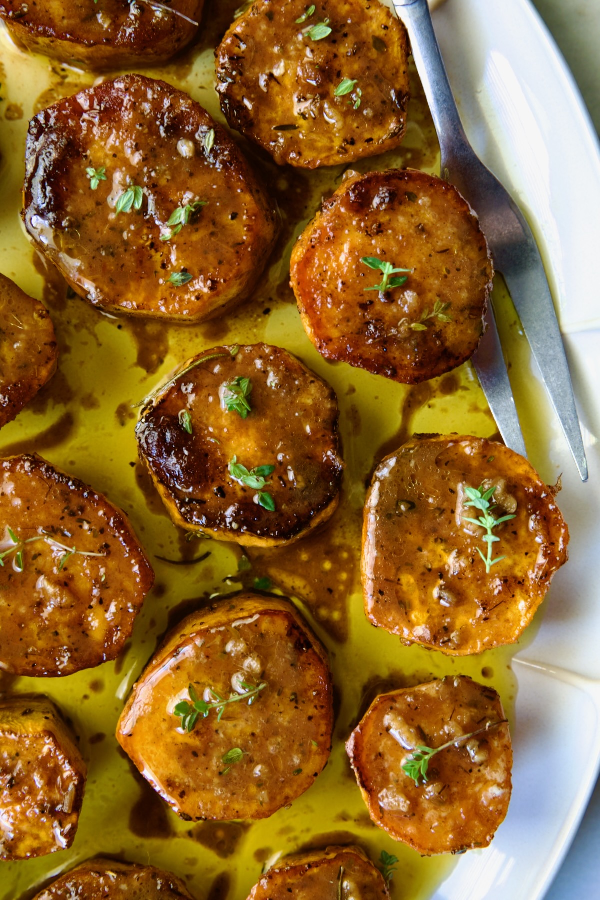 Fondant Sweet Potatoes garnished with fresh thyme on white oval platter.