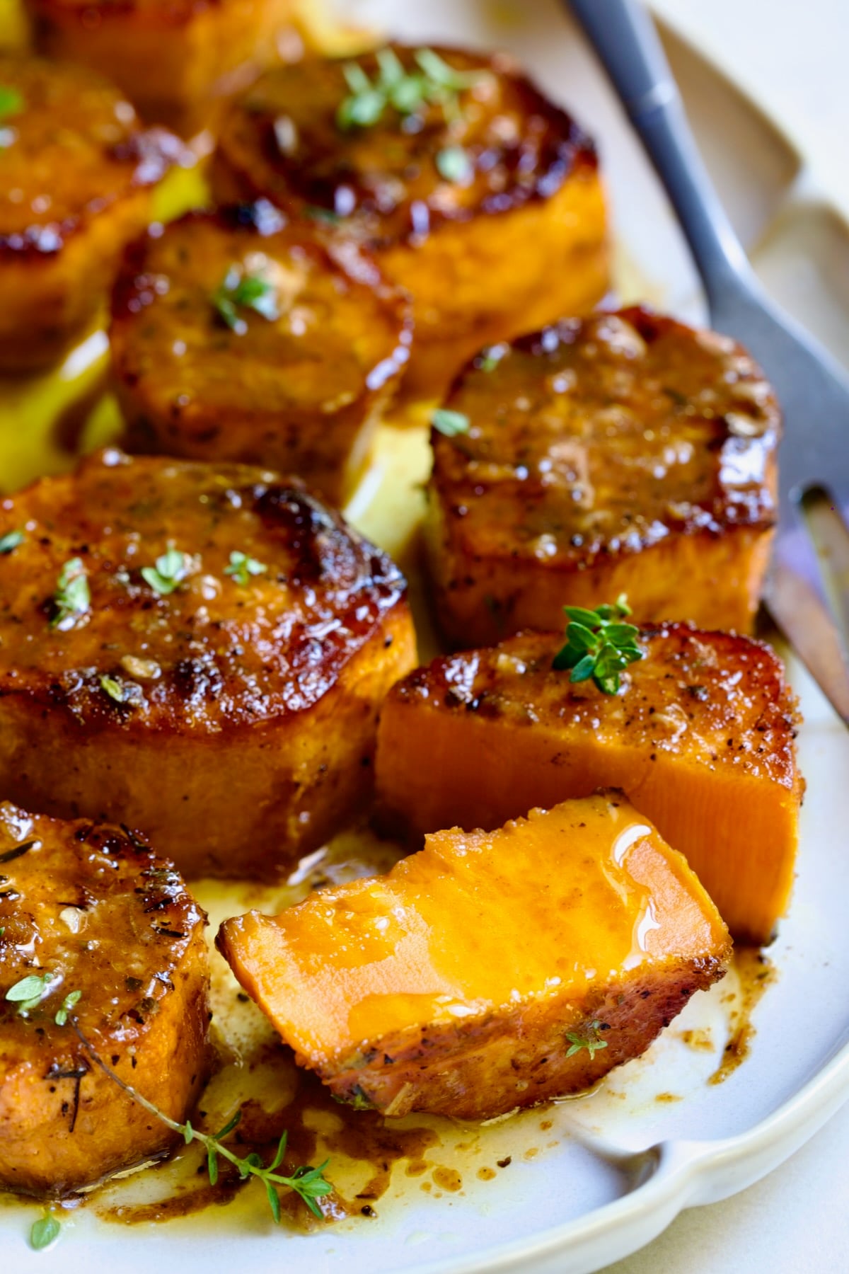 Fondant Sweet Potatoes garnished with fresh thyme on white oval platter with one cut in half.