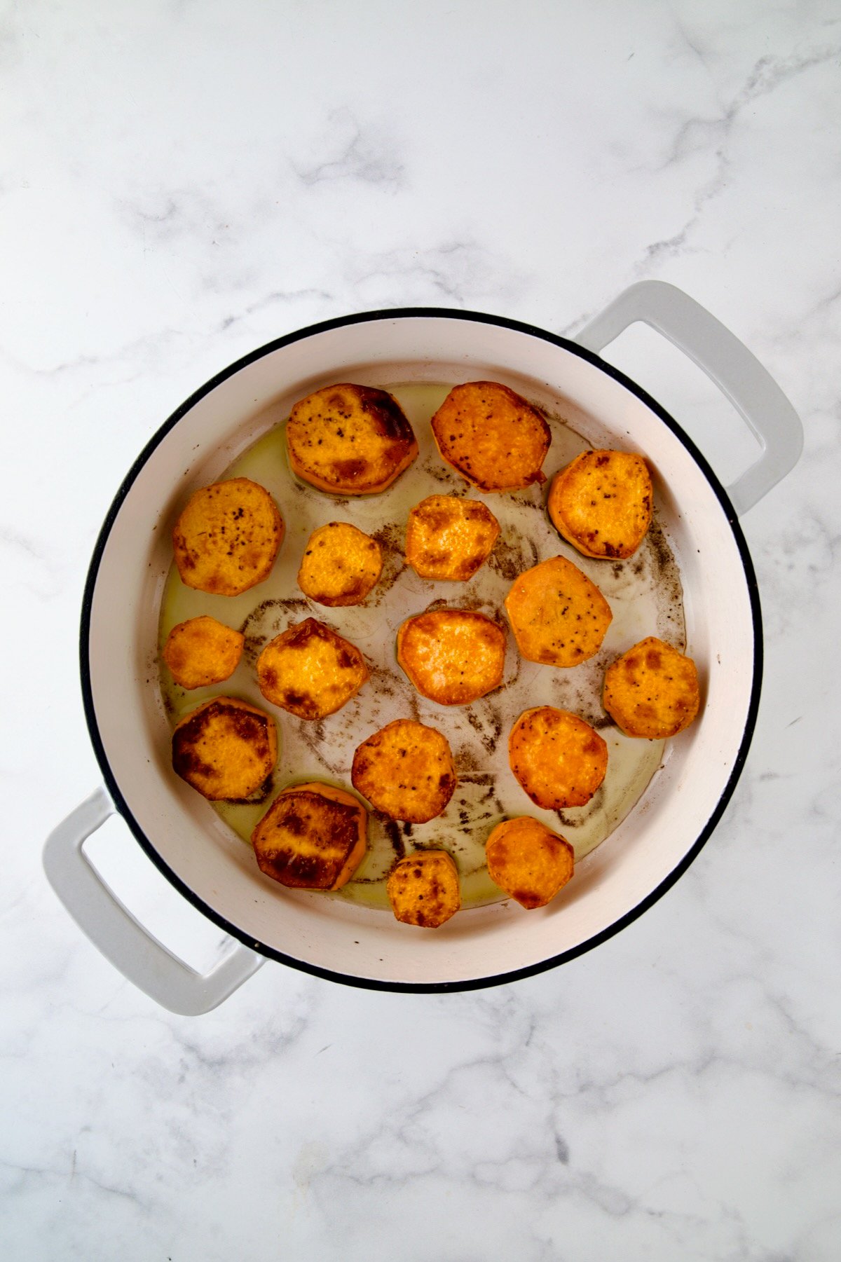 Rounds of sweet potatoes in white enamel cast iron skillet after being browned.