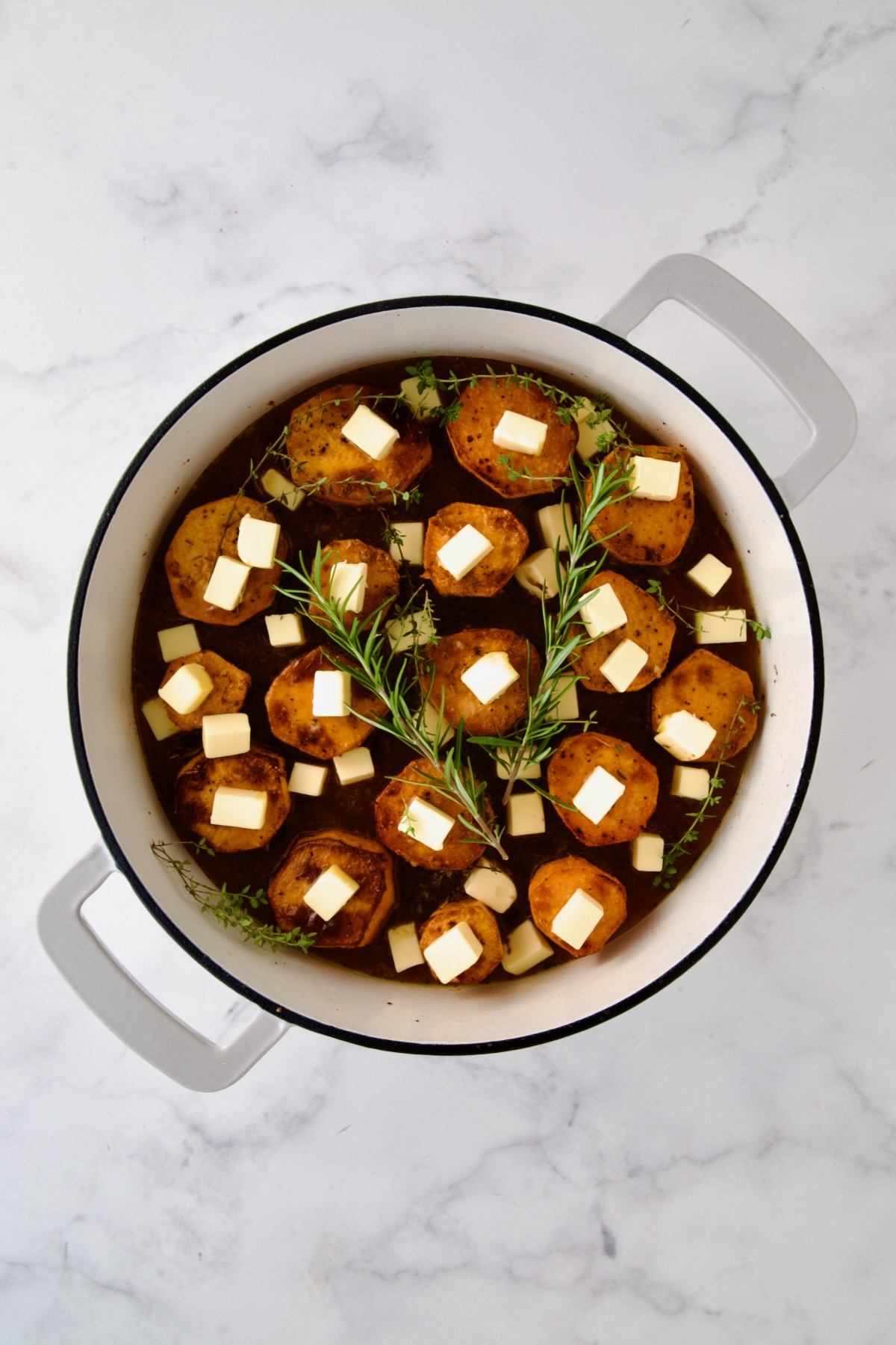 Butter and herbs added to browned sweet potato rounds in white enamel cast iron skillet.