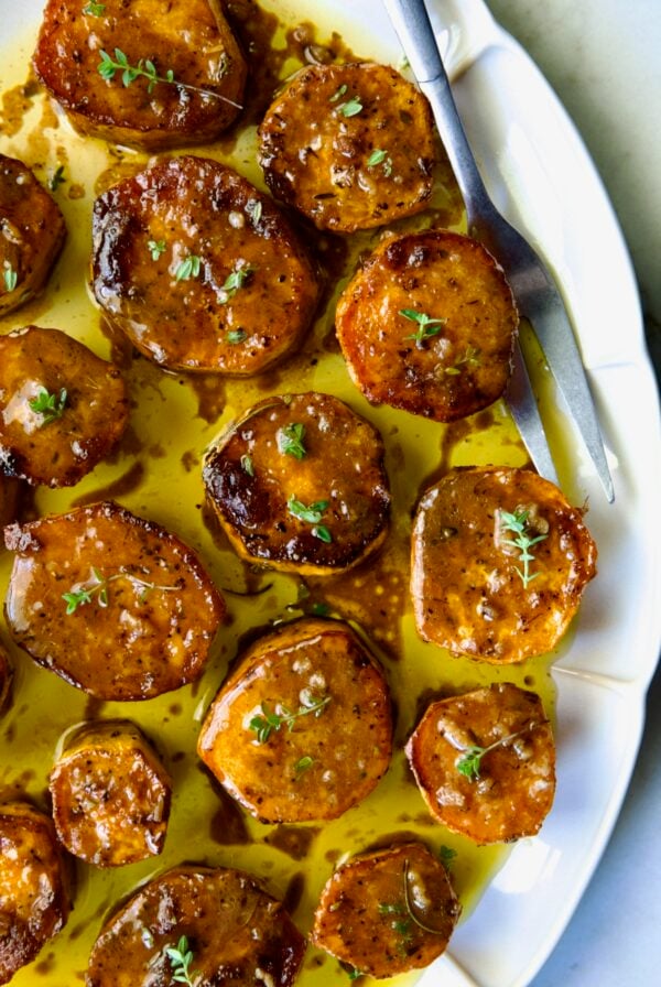 Fondant Sweet Potatoes garnished with fresh thyme on white oval platter.