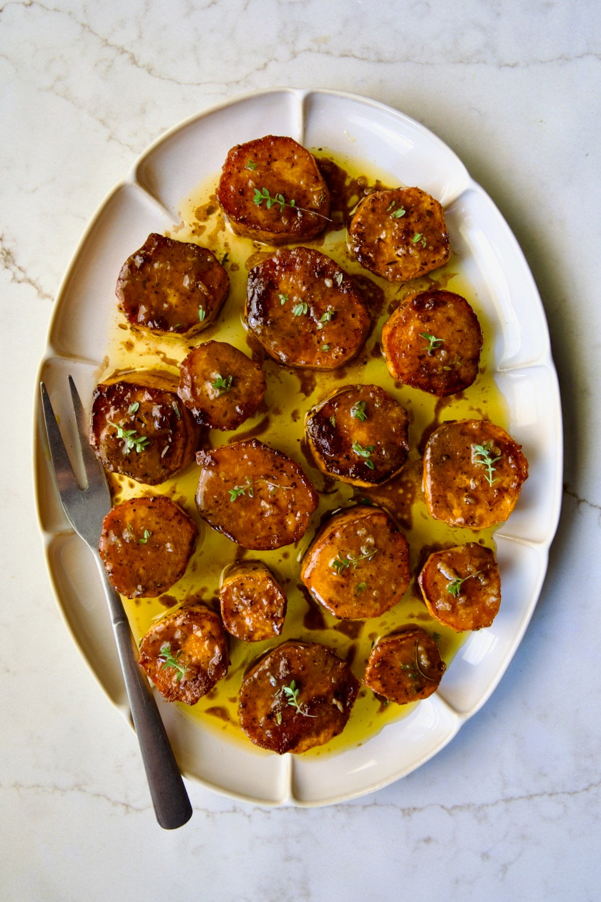 Fondant Sweet Potatoes garnished with fresh thyme on white oval platter.