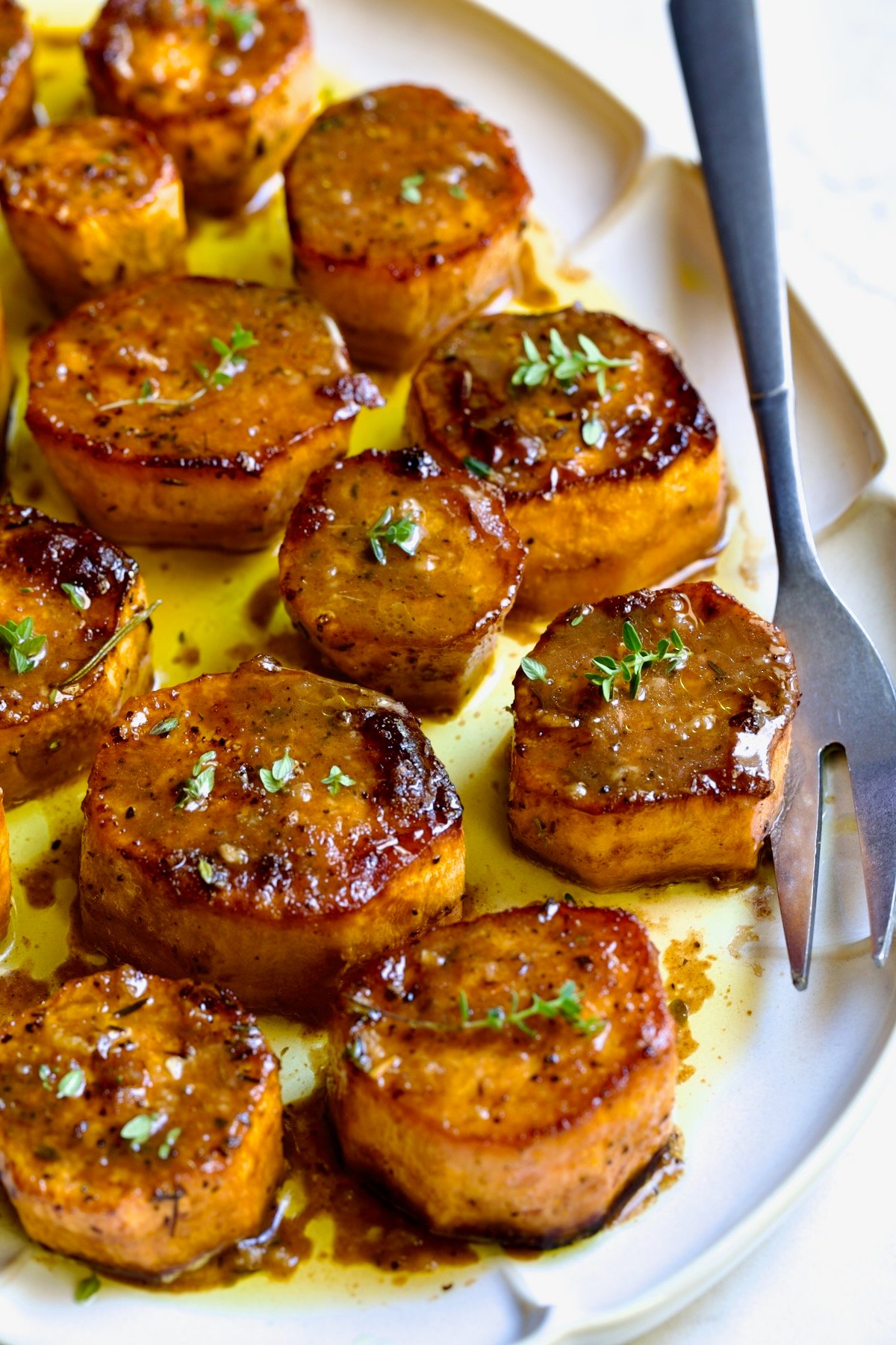 Fondant Sweet Potatoes garnished with fresh thyme on white oval platter.