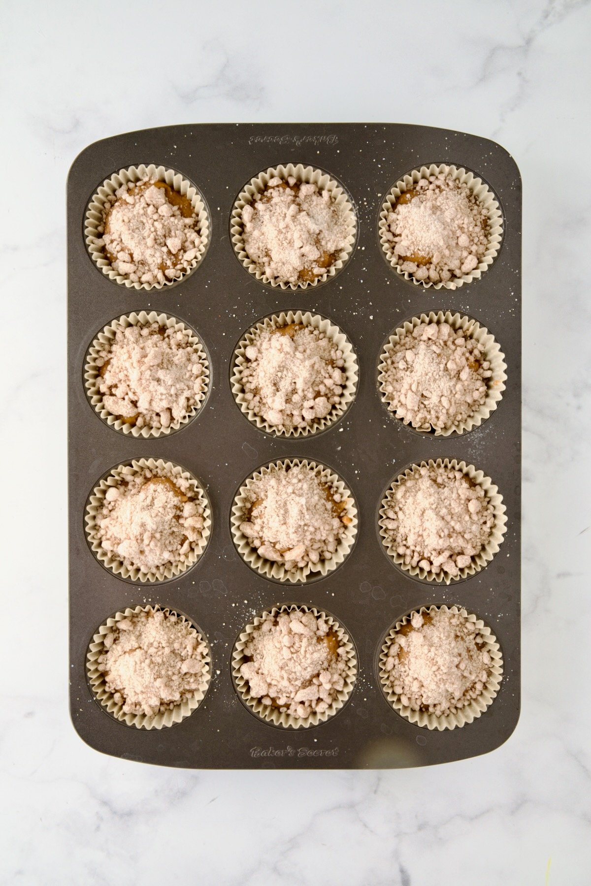 Batter for muffins in a 12-cup muffin pan after the streusel is added.