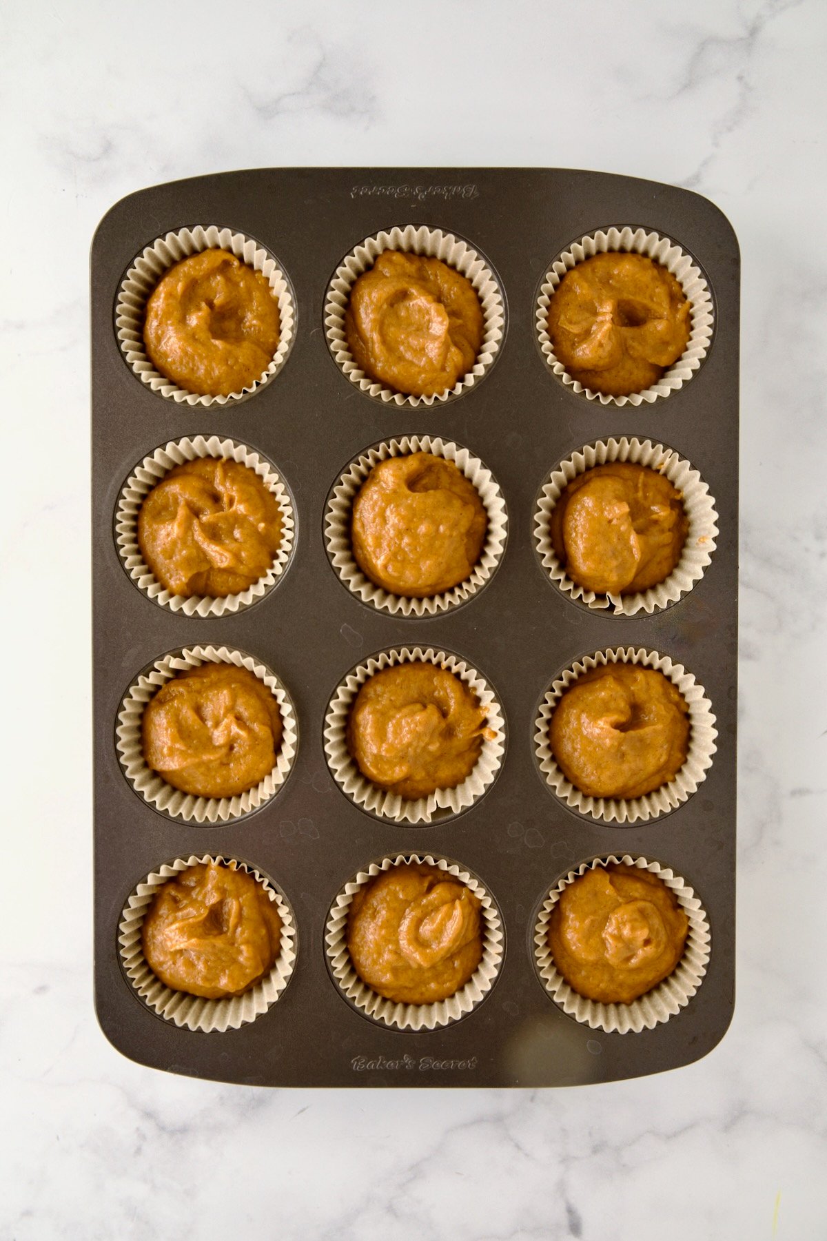 Batter for muffins in a 12-cup muffin pan before the streusel is added.