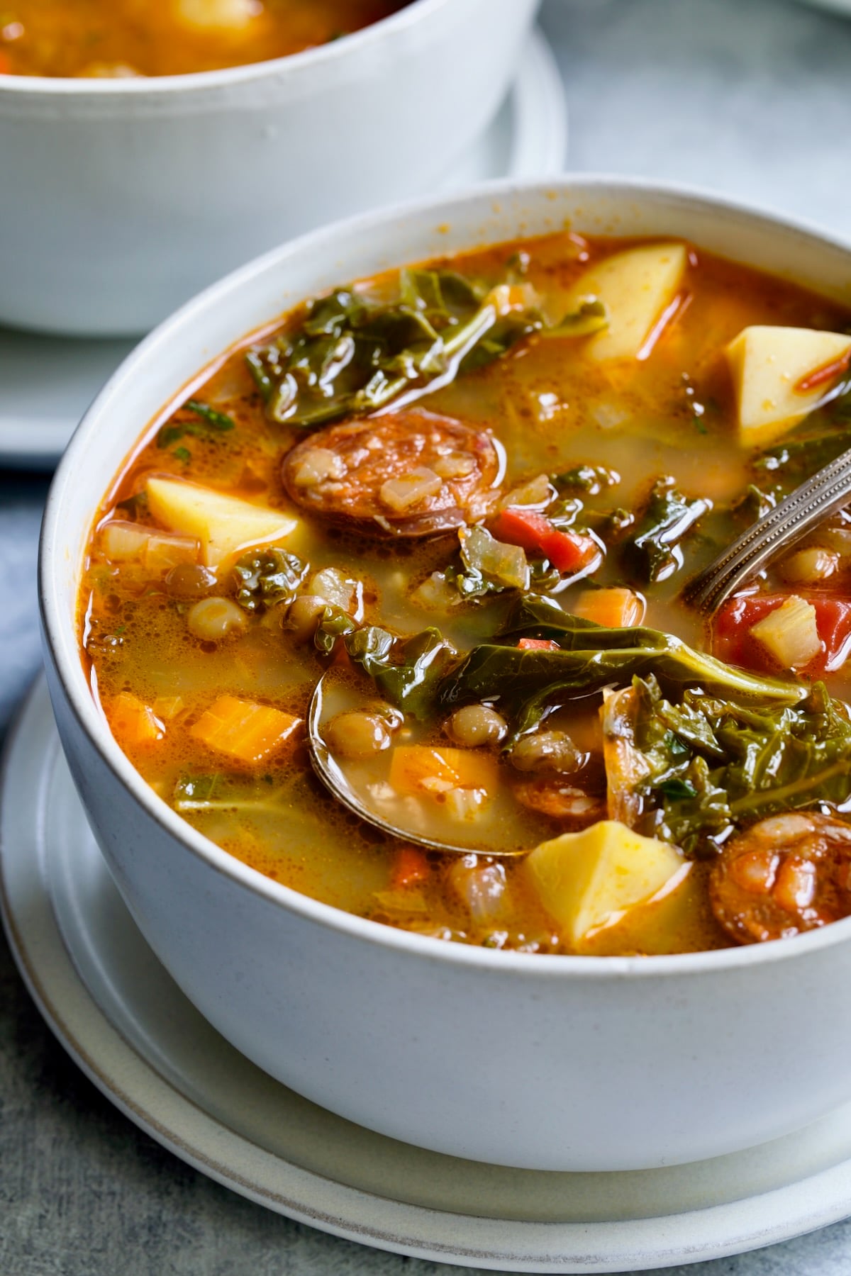 One serving of Spanish Lentil Potato Soup in white bowl with soup spoon.