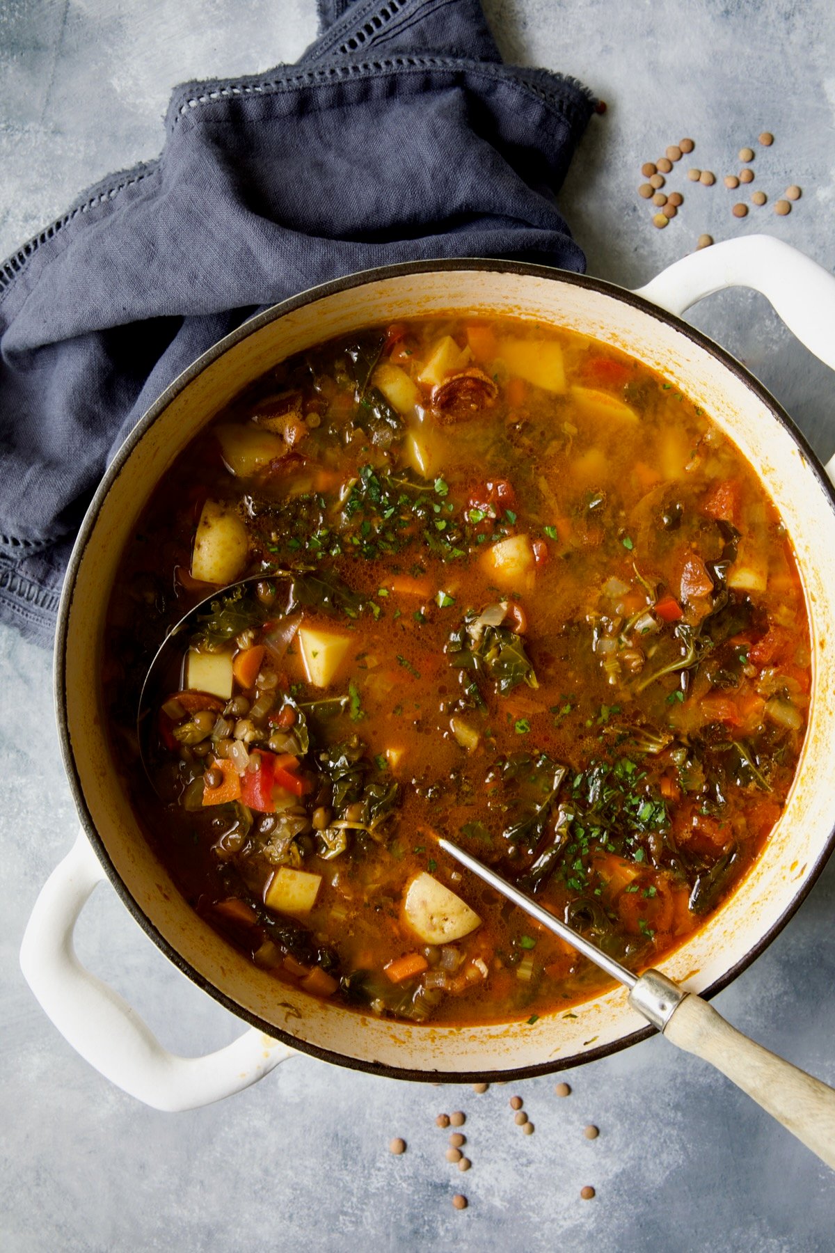 Finished Spanish Lentil Potato Soup in white enamel Dutch oven with soup ladle.