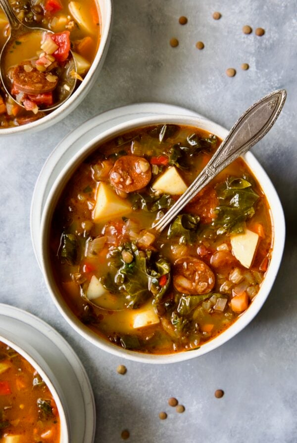 One serving of Spanish Lentil Potato Soup in white bowl with soup spoon with lentils scattered about.